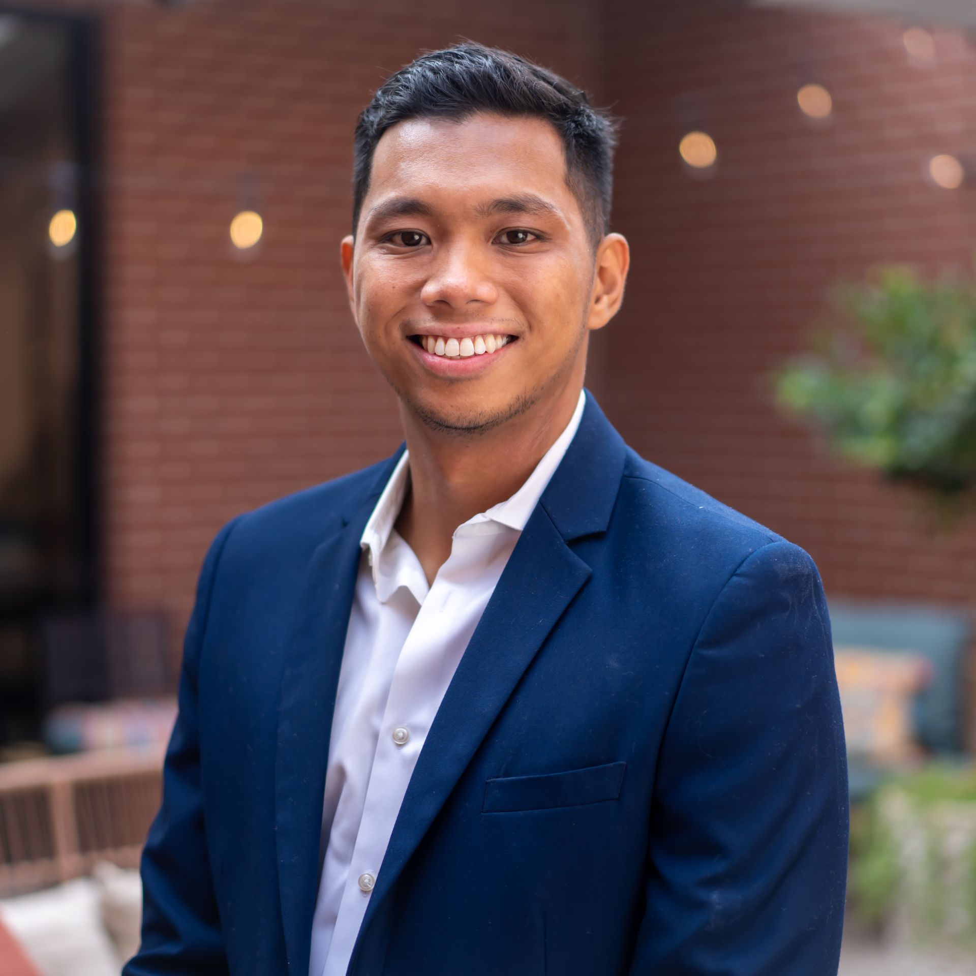 Man in blue blazer and white shirt smiles outdoors.