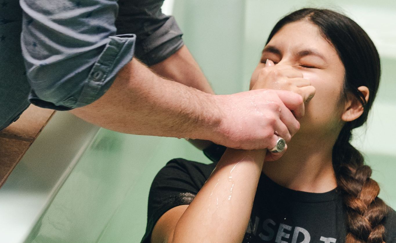 Person being baptized in water, hands held by another person.