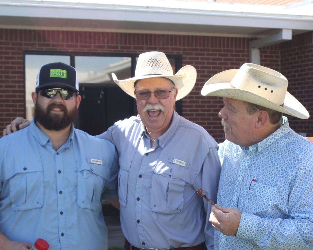 Three men in cowboy hats smile, posing outside a building.