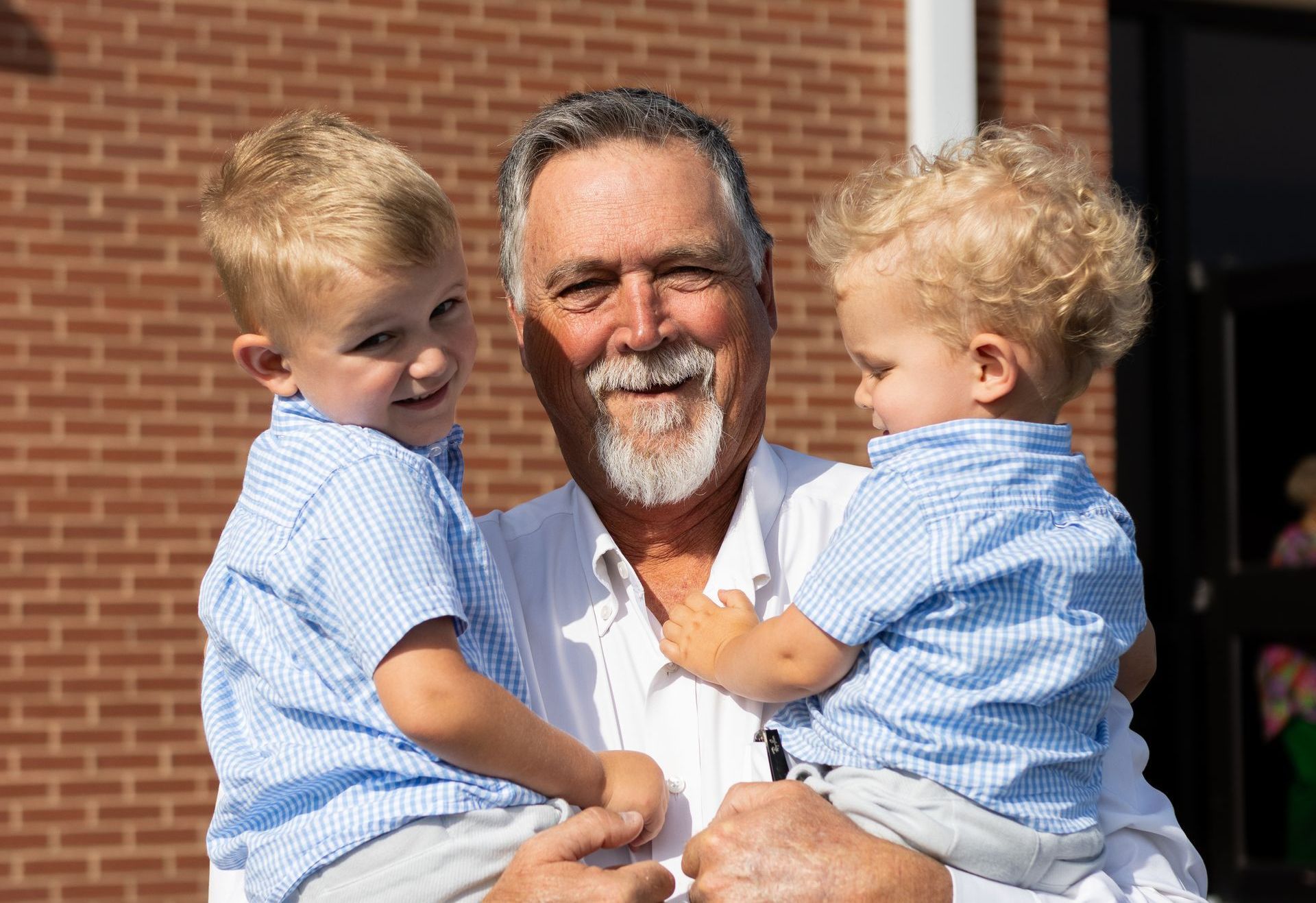 Man holding two young boys in front of a brick building; they wear blue and white striped shirts.