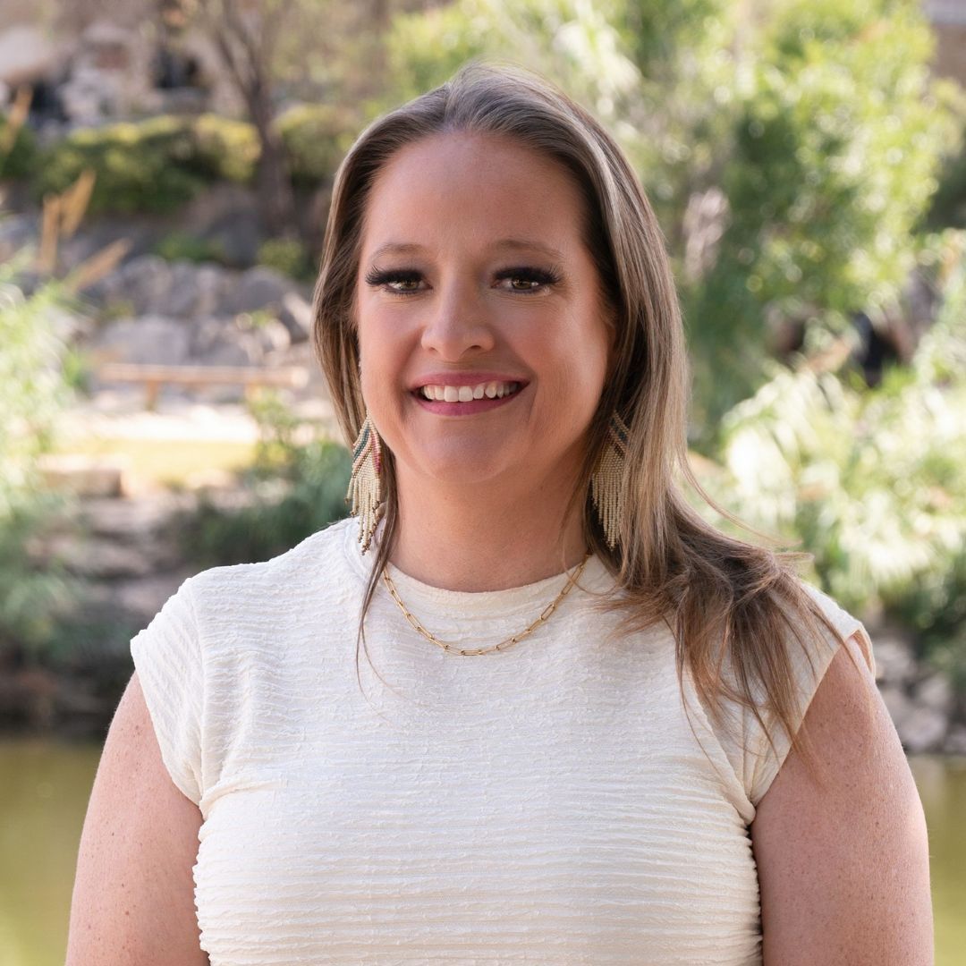 Man with glasses in blue floral shirt, looking off-camera. Outdoors, brick background.