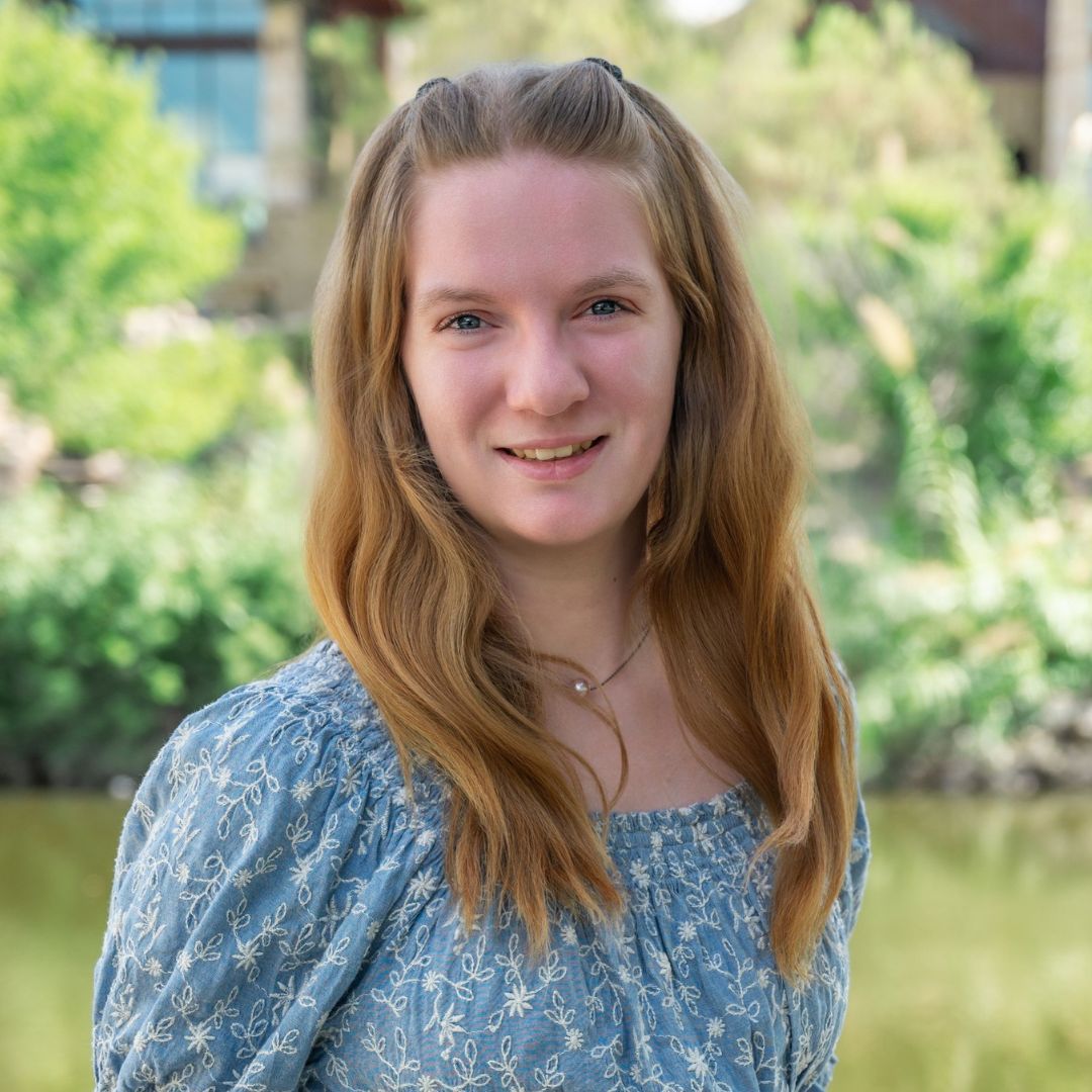 Man with glasses in blue floral shirt, looking off-camera. Outdoors, brick background.