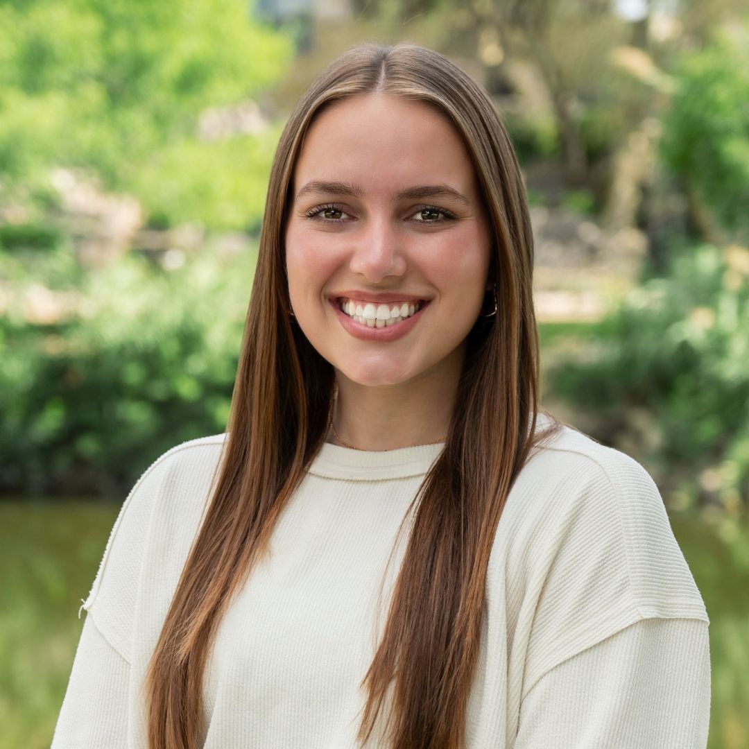 Man with glasses in blue floral shirt, looking off-camera. Outdoors, brick background.