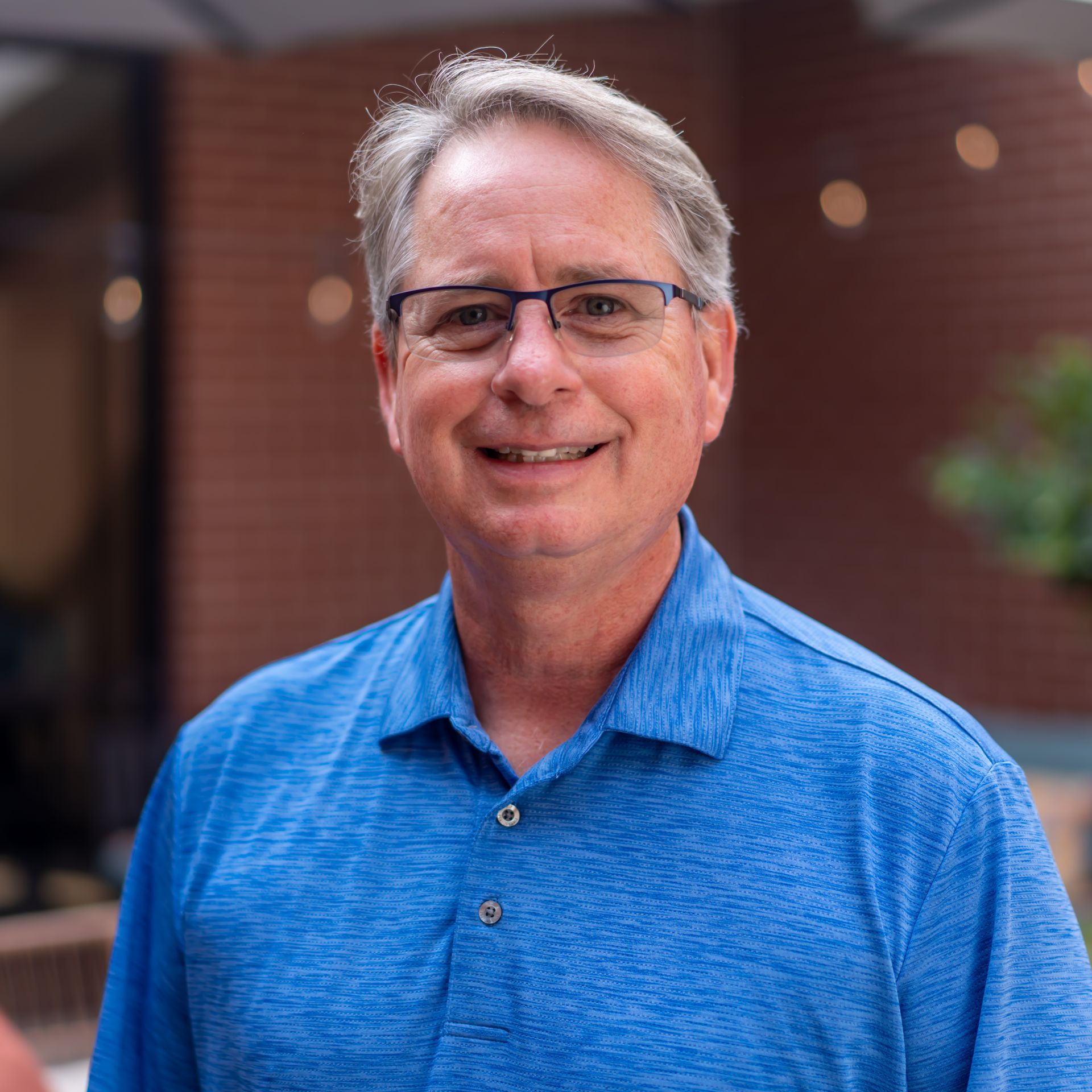 Man wearing glasses and a blue shirt smiles outdoors.