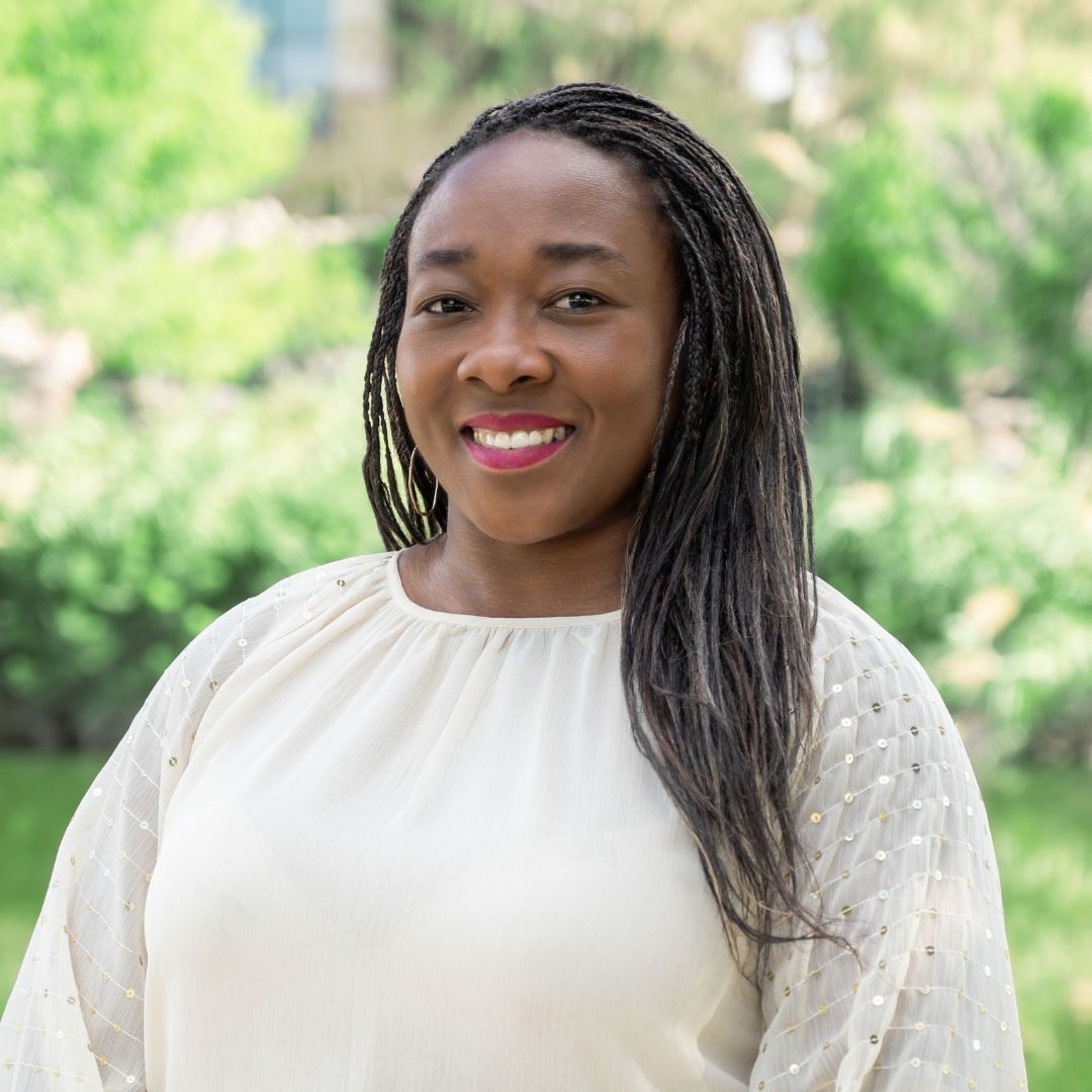 Bald man with glasses wearing a blue shirt with a white cross. Smiling outdoors near brick wall.