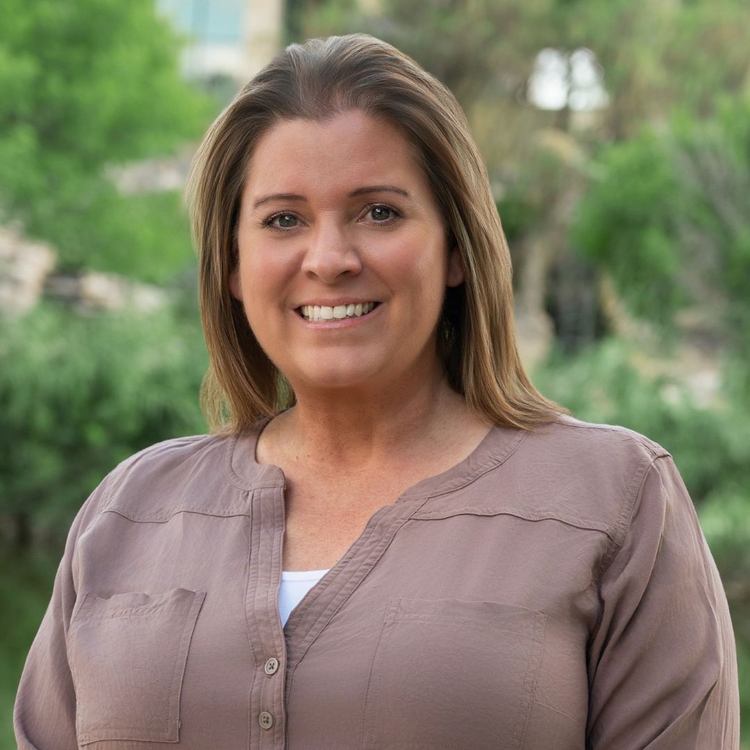Woman in blue top smiles outdoors, brick backdrop, decorative sleeves.