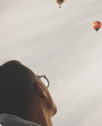 Person looking up at hot air balloons in a cloudy sky.