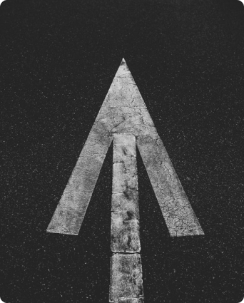 White upward-pointing arrow painted on black asphalt surface.