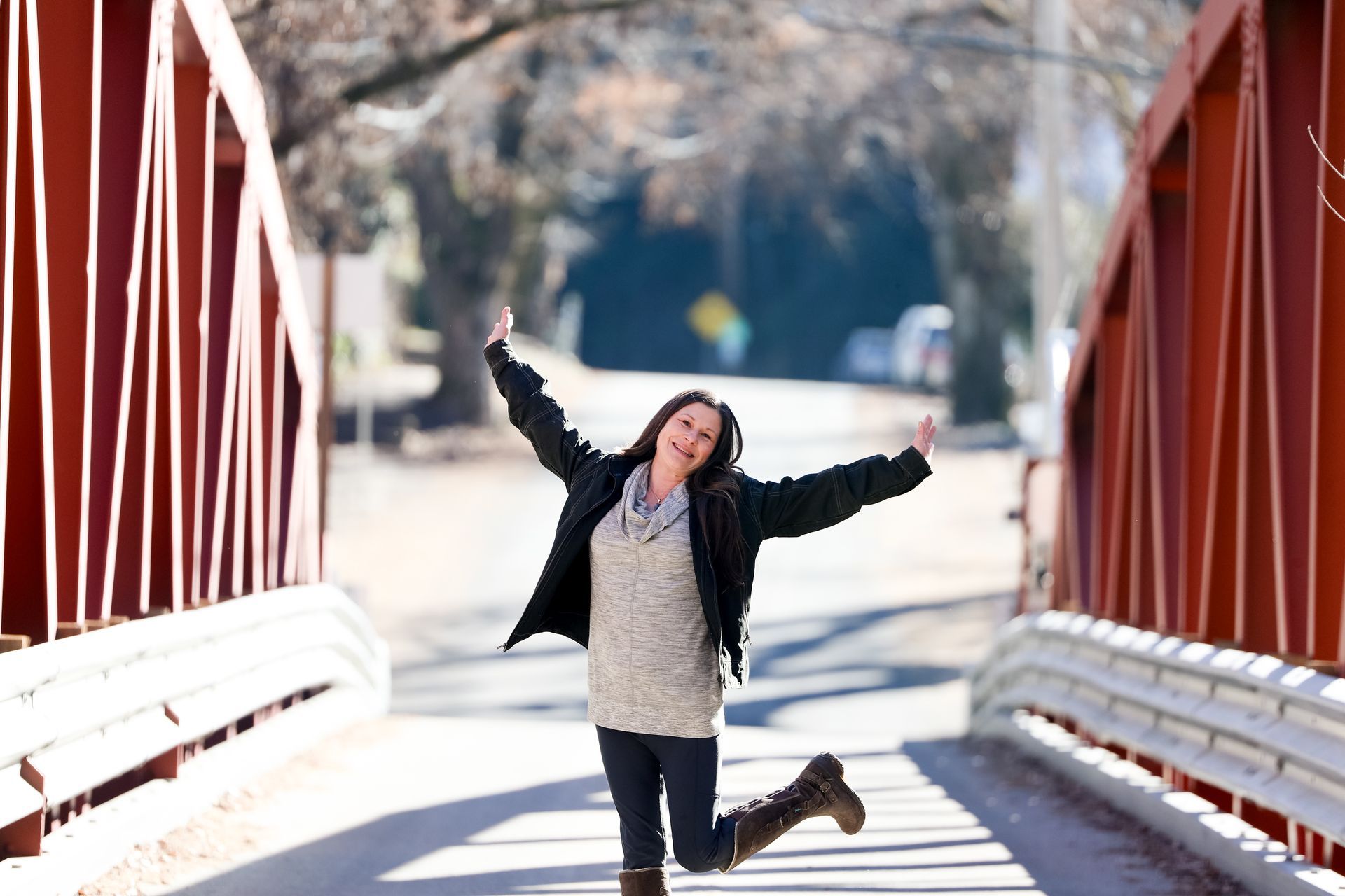 A woman is jumping in the air on a bridge with her arms outstretched.