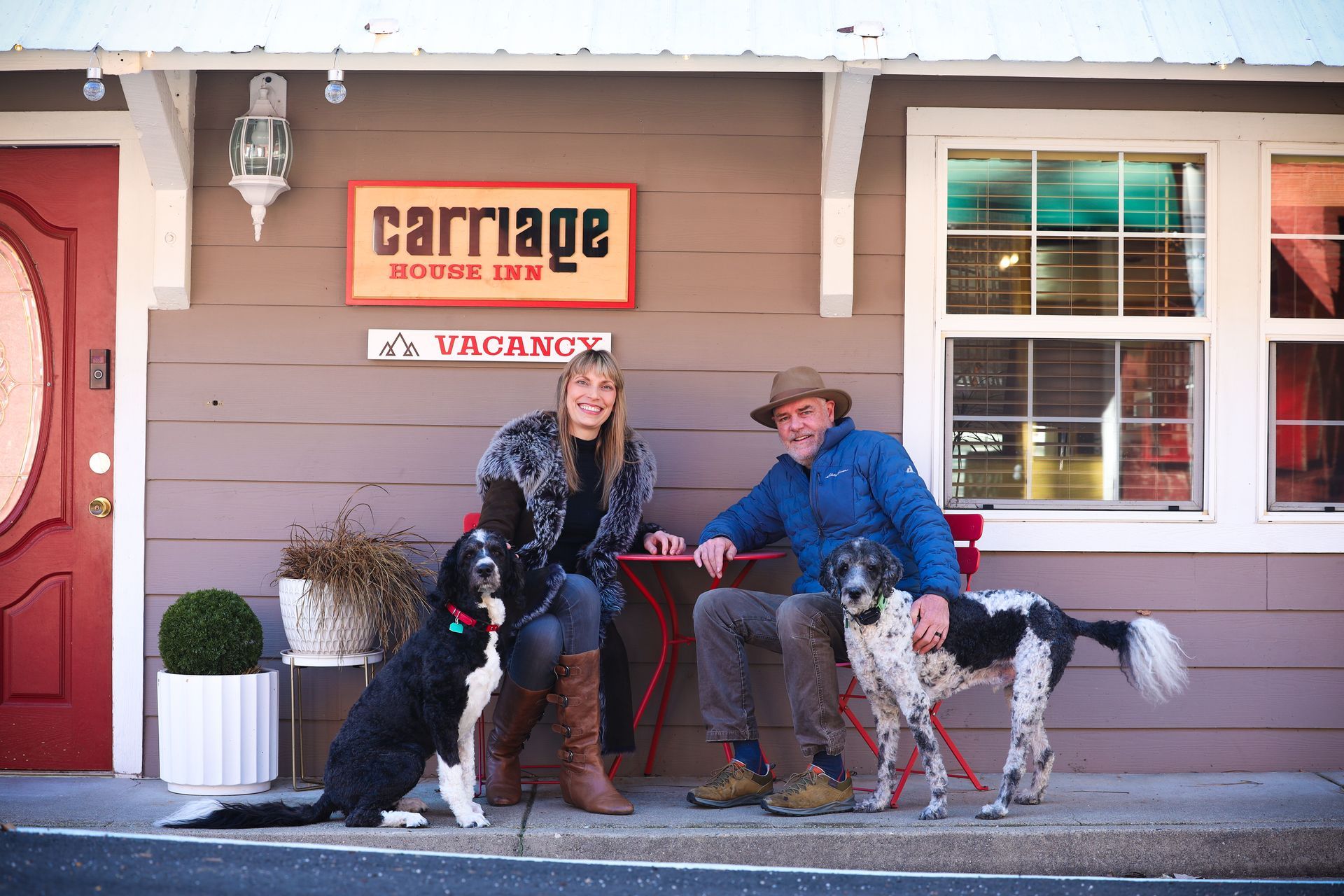 A man and a woman are sitting on a bench with their dogs.