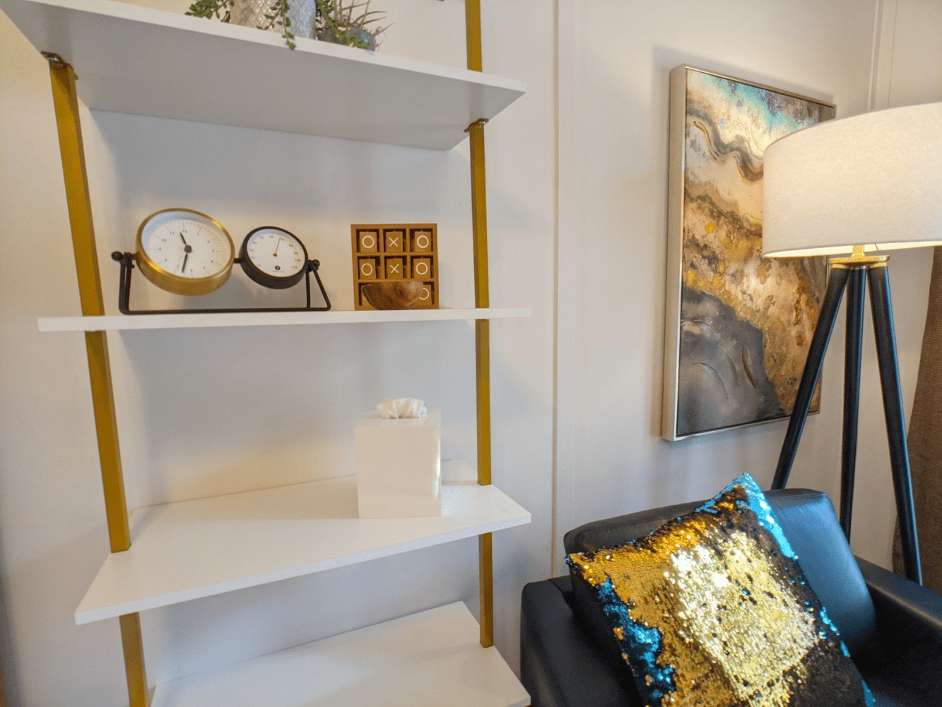 A living room with a chair , shelf , lamp and painting on the wall.