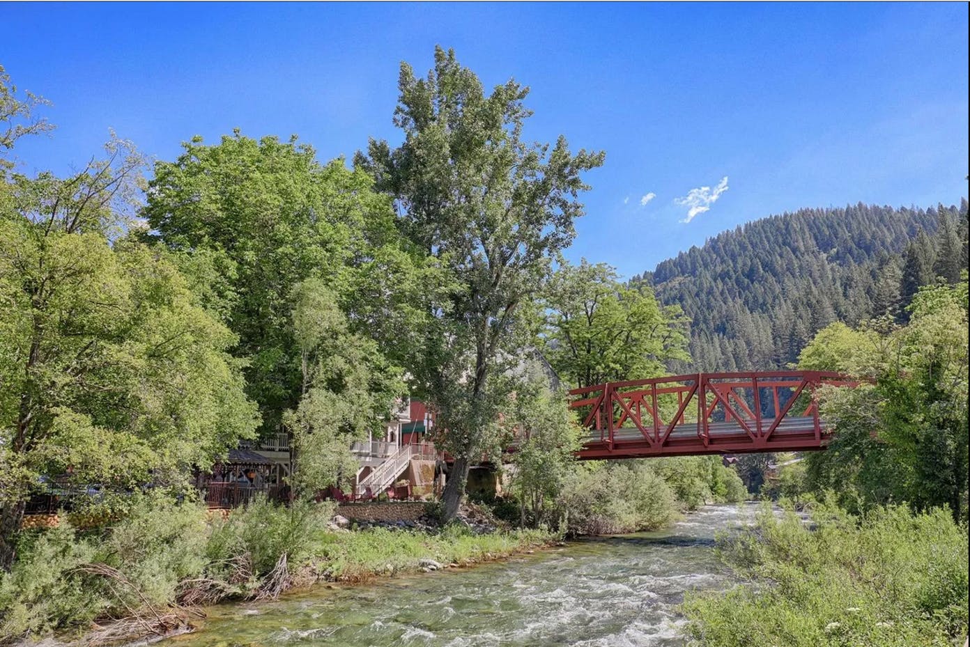 A red bridge over a river surrounded by trees and mountains.