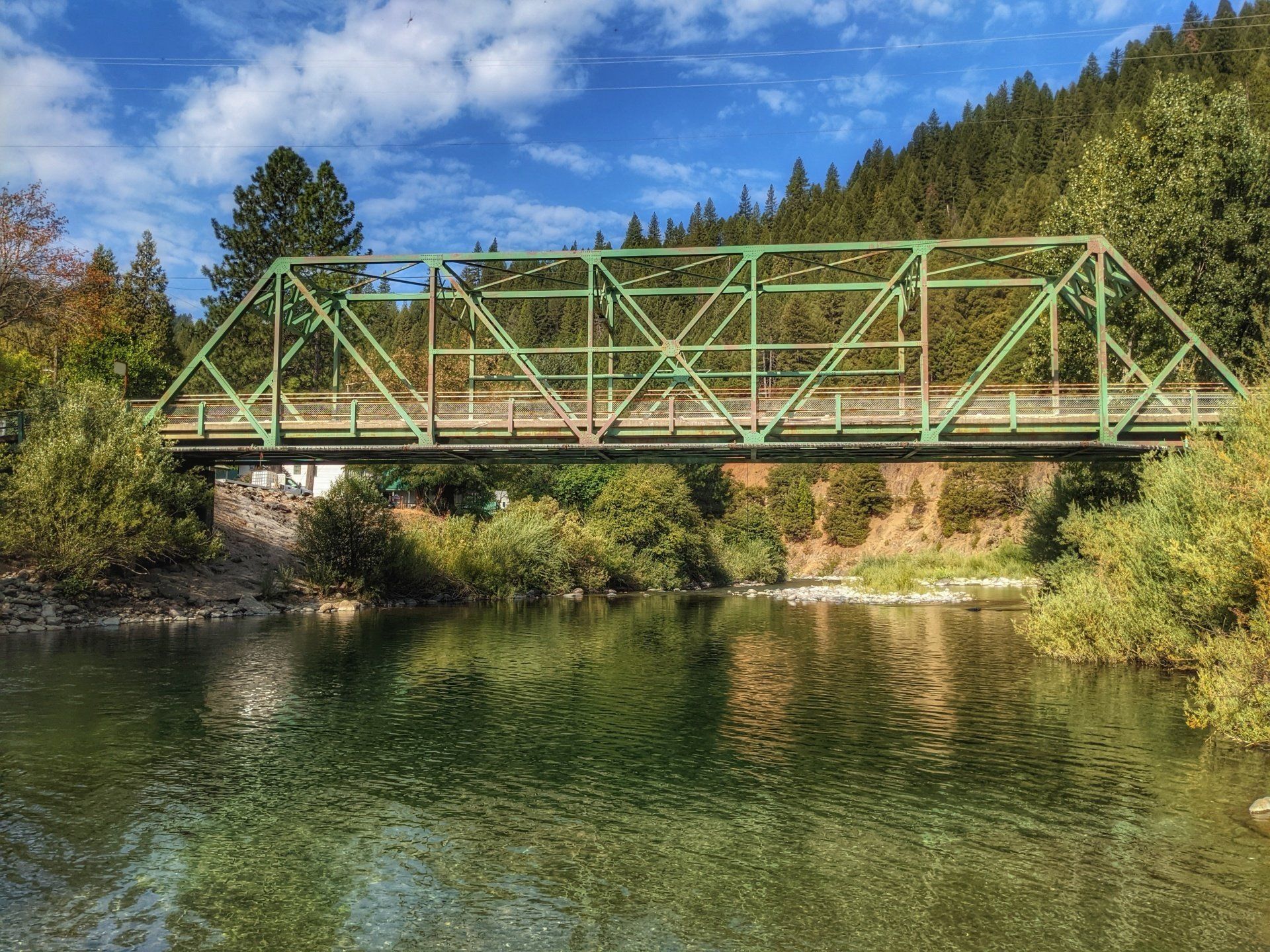 A green bridge over a river with trees in the background.