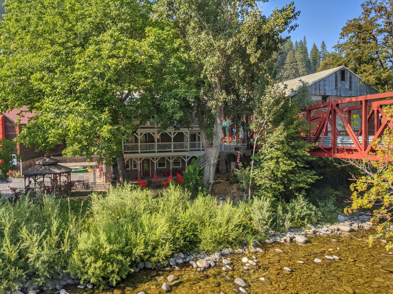 A red bridge over a river with a house in the background.