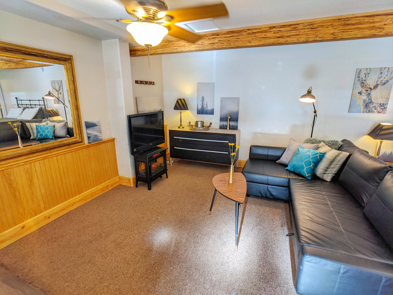 A living room with a couch , television , mirror and ceiling fan.