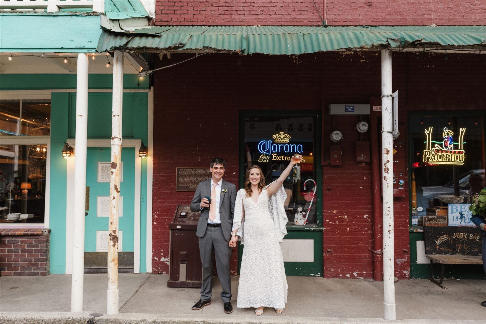 A bride and groom are standing in front of a building holding hands.