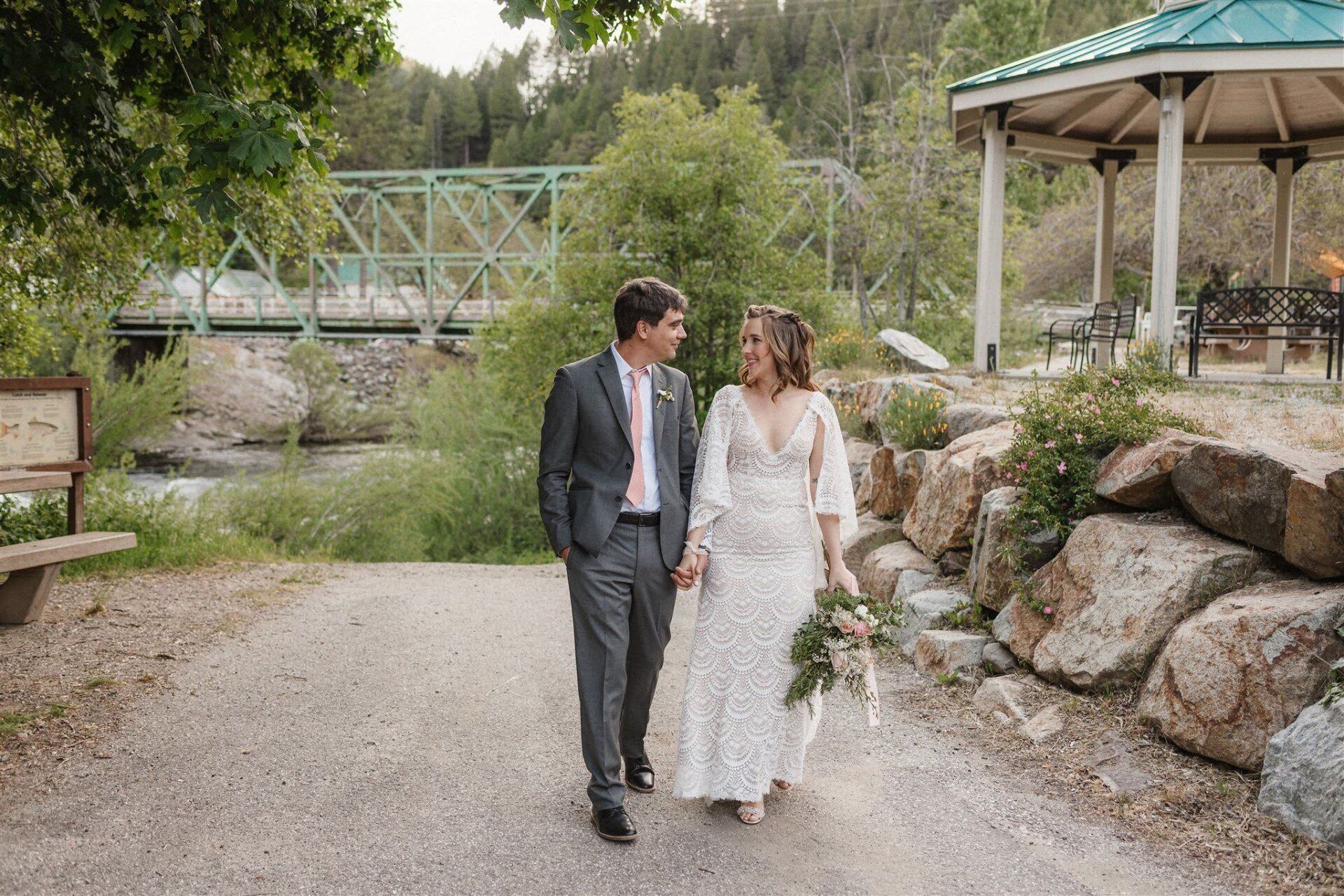 A bride and groom are walking down a path holding hands.