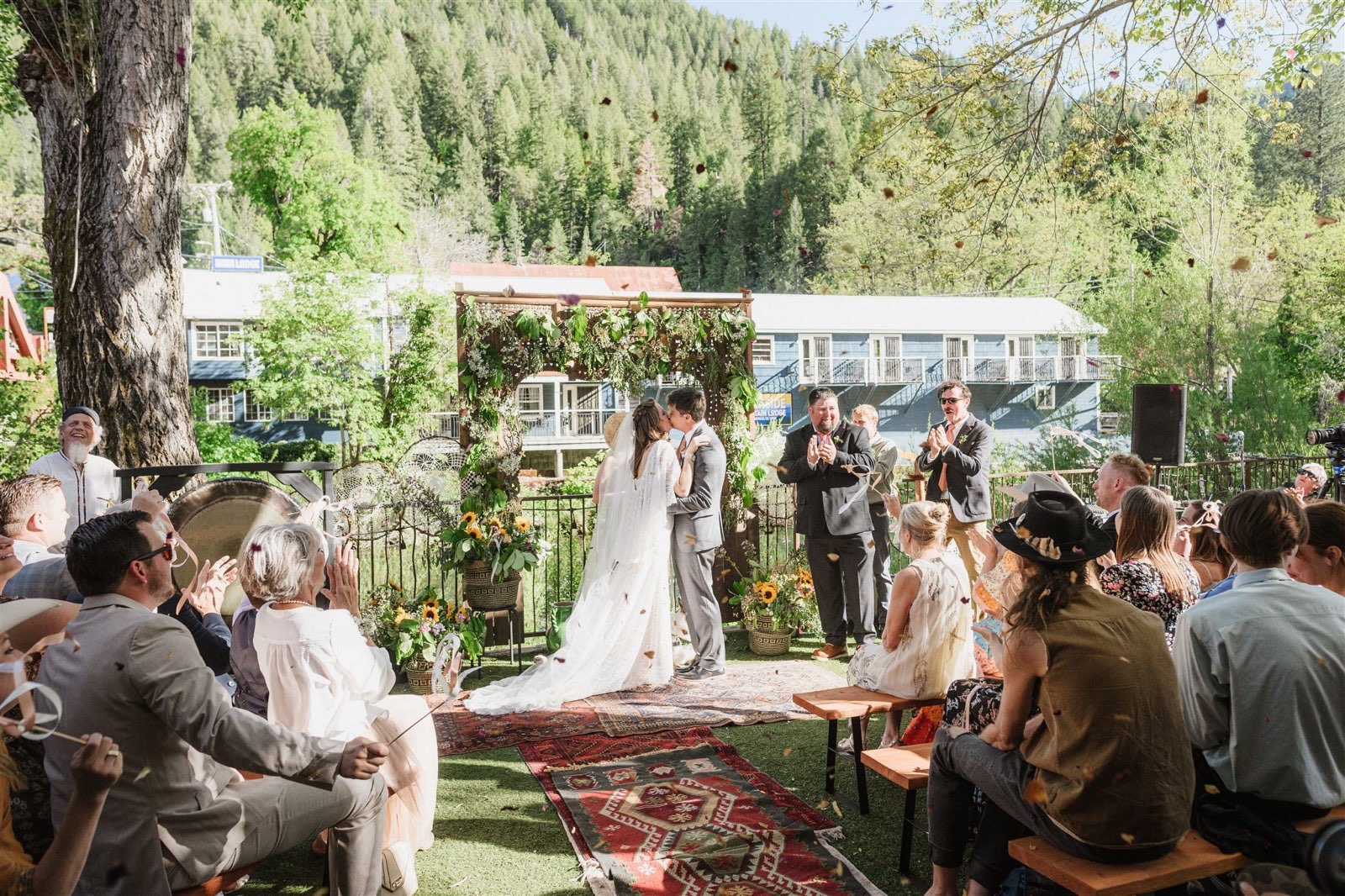 A bride and groom are kissing during their wedding ceremony while their guests watch.