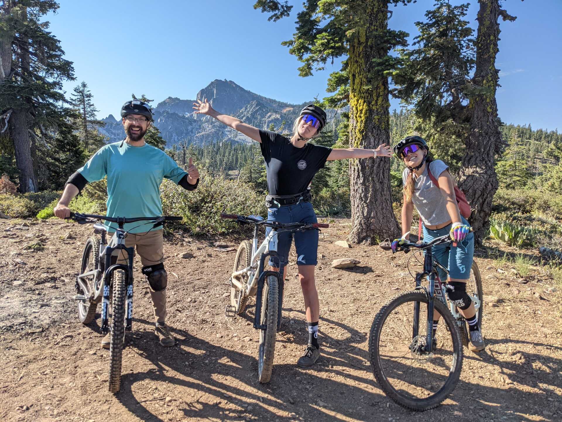 Three people are standing next to each other on bicycles on a dirt road.