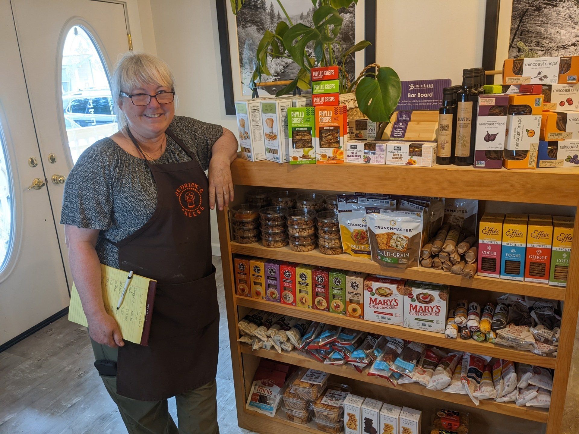 A woman in an apron is leaning against a shelf in a store.