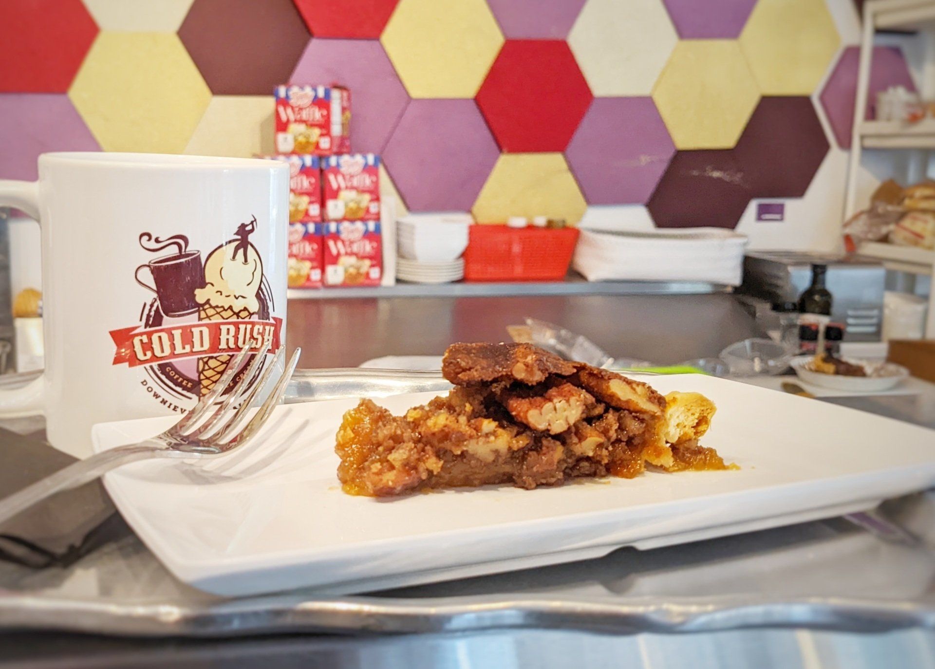 A white plate with a slice of pie on it next to a mug that says cold nuts