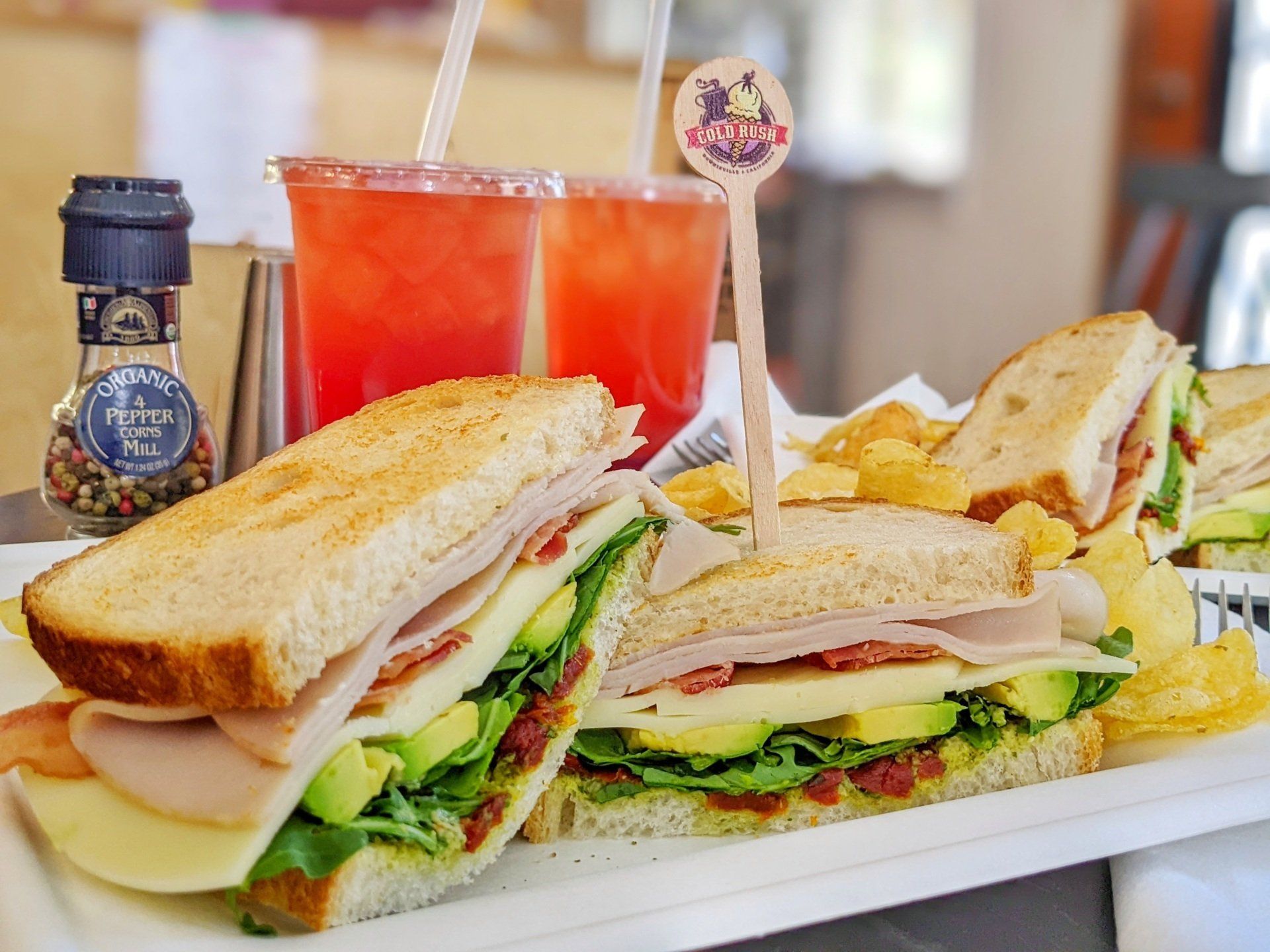 A club sandwich is sitting on a white plate next to a drink.