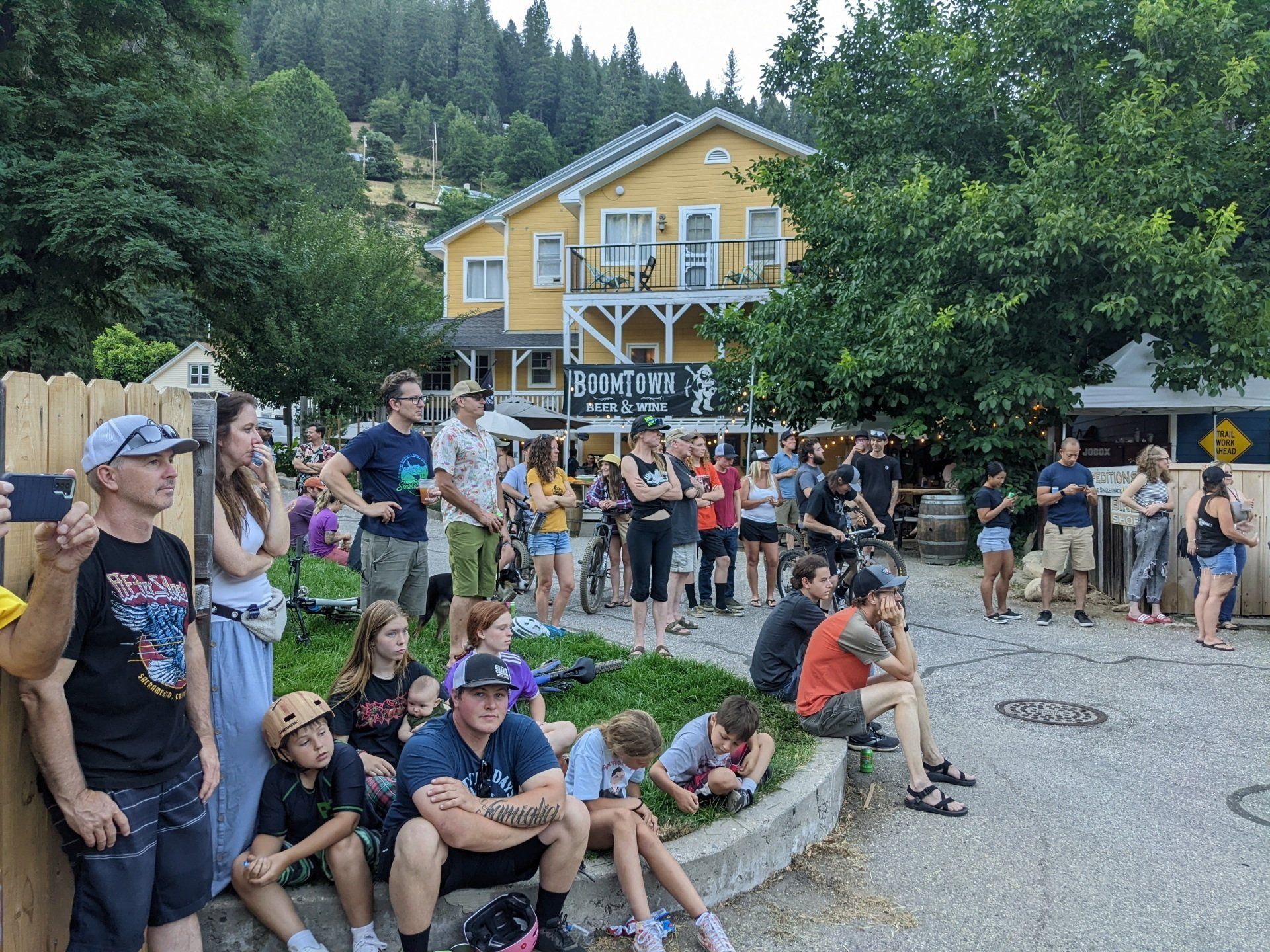 A group of people are sitting on a sidewalk in front of a yellow building.