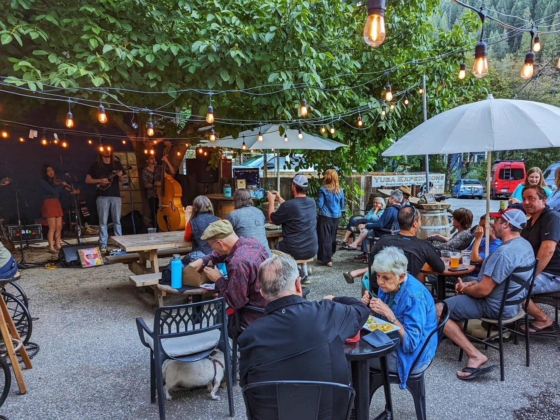 A group of people are sitting at tables outside under umbrellas.