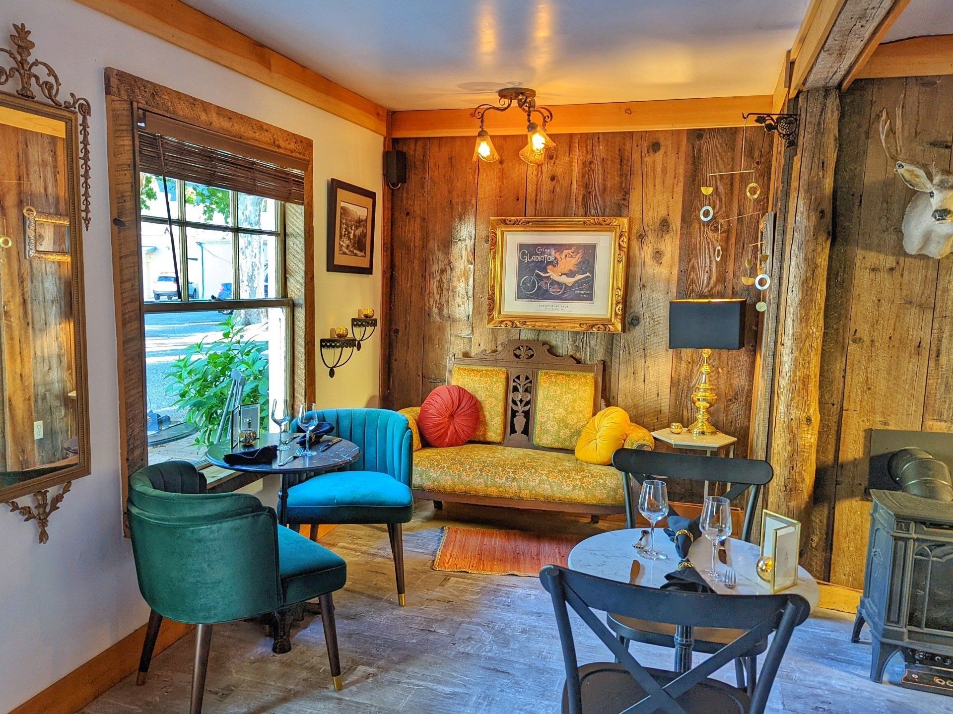 A living room with a couch , chairs , tables and a deer head on the wall.