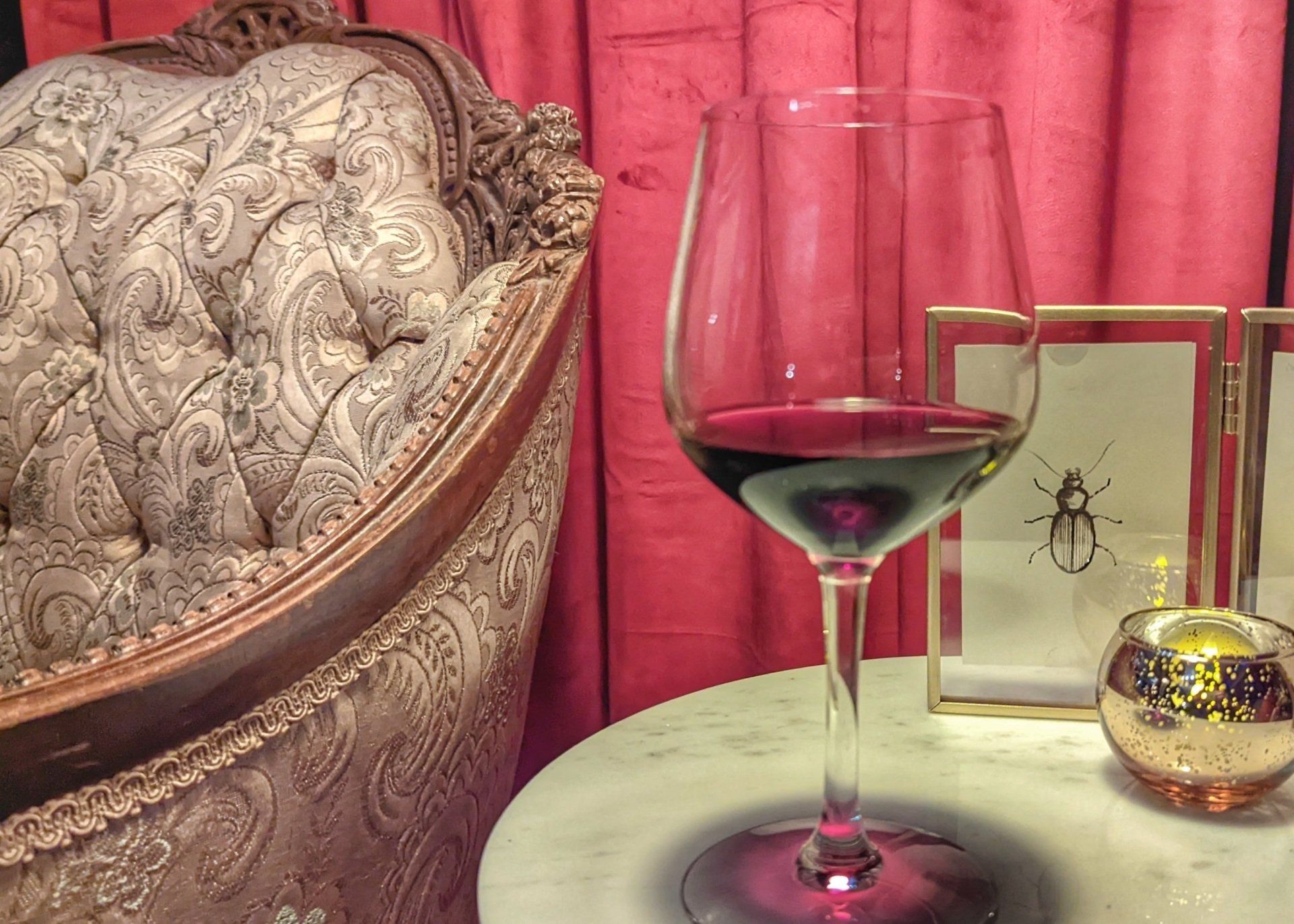 A glass of wine is sitting on a table next to a chair.