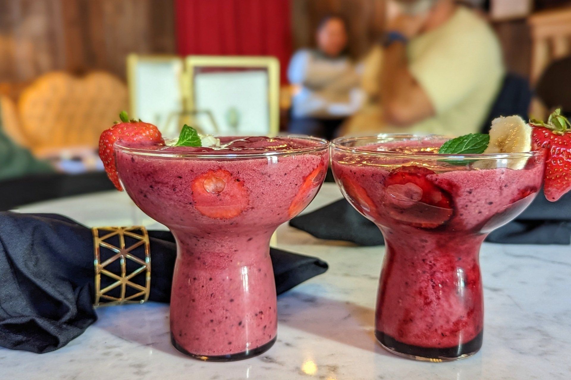 Two glasses of smoothies with strawberries and bananas on a table.