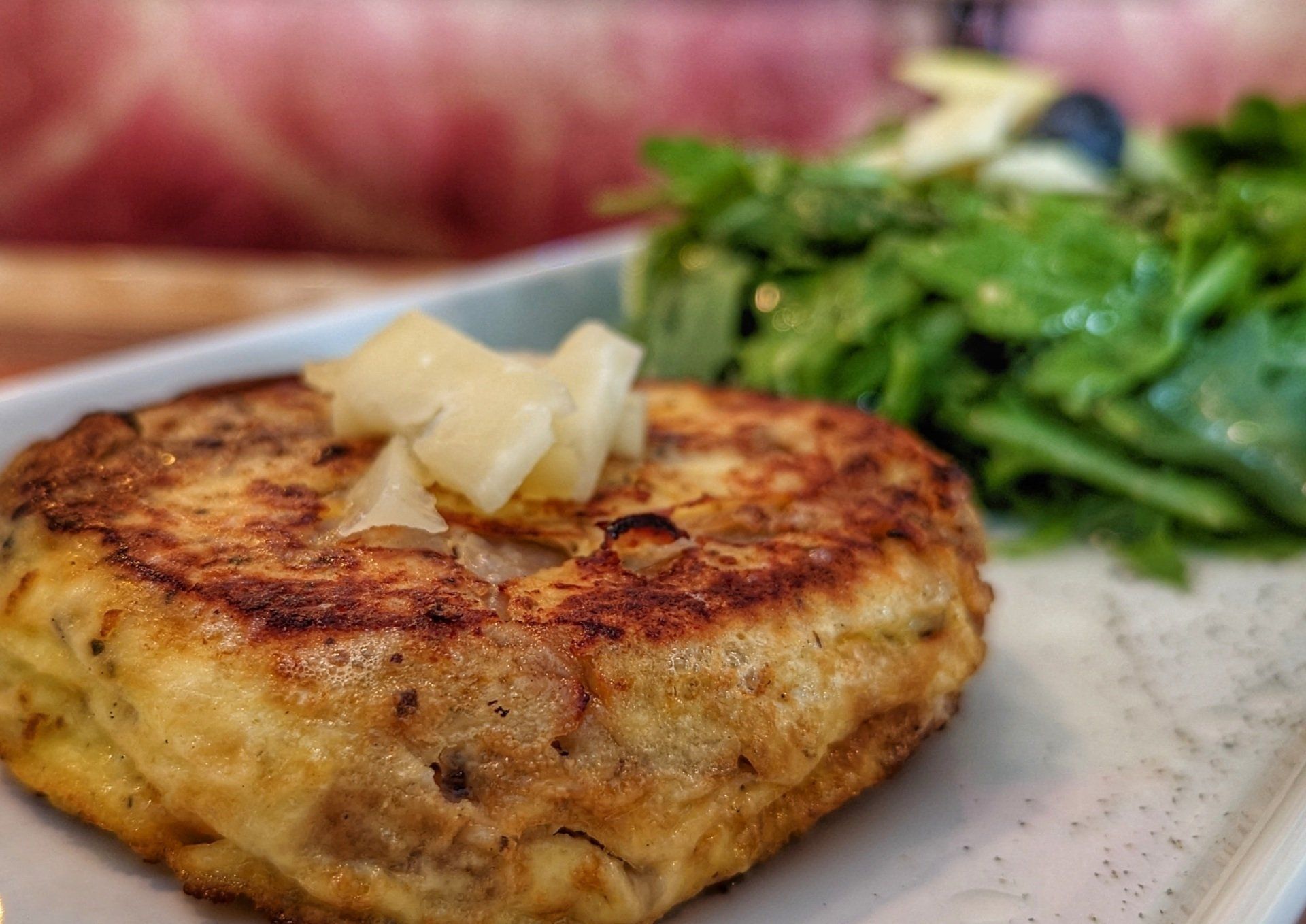 A close up of a crab cake on a plate with a salad.