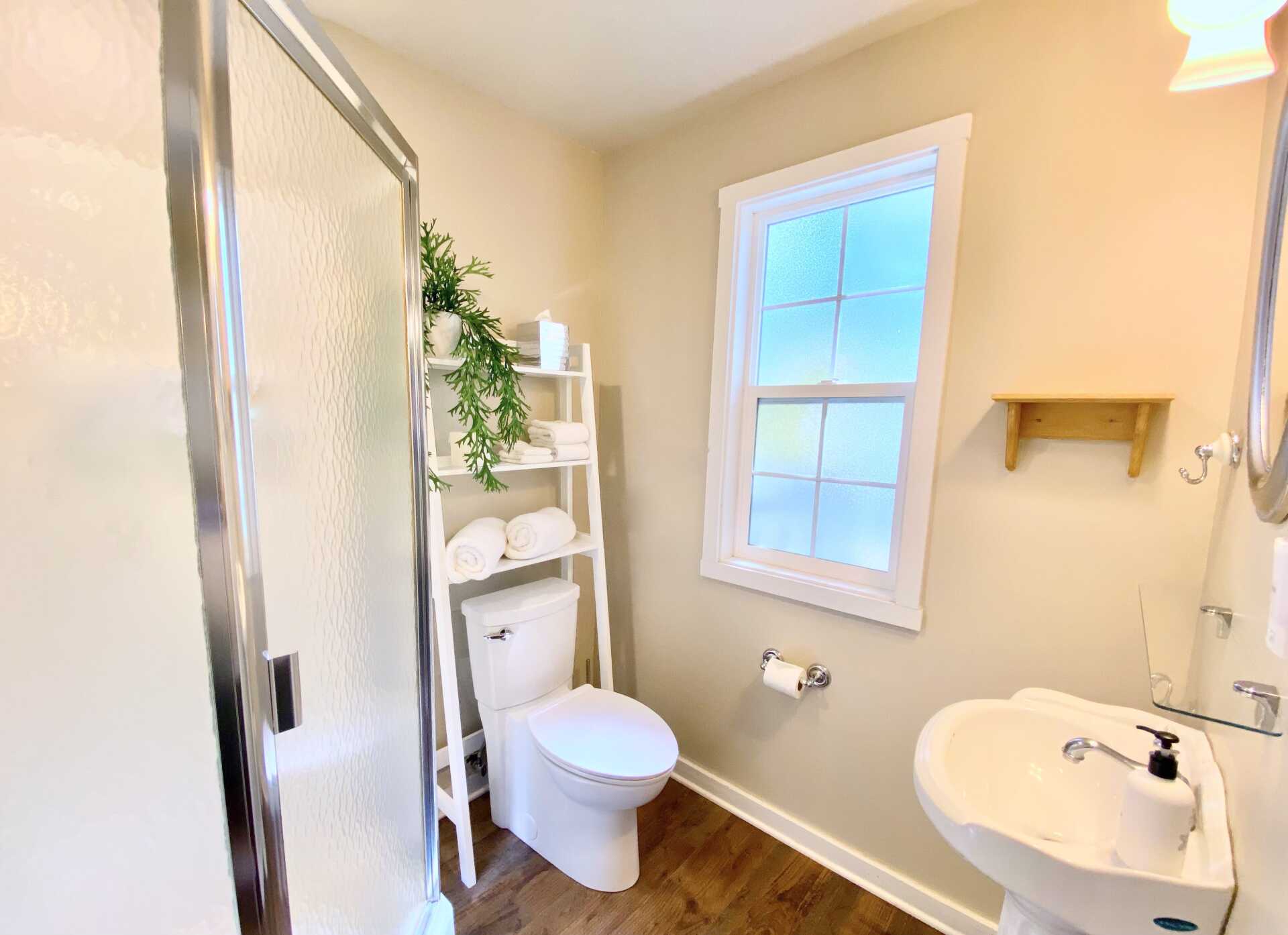 A bathroom with a toilet , sink , shower and window.