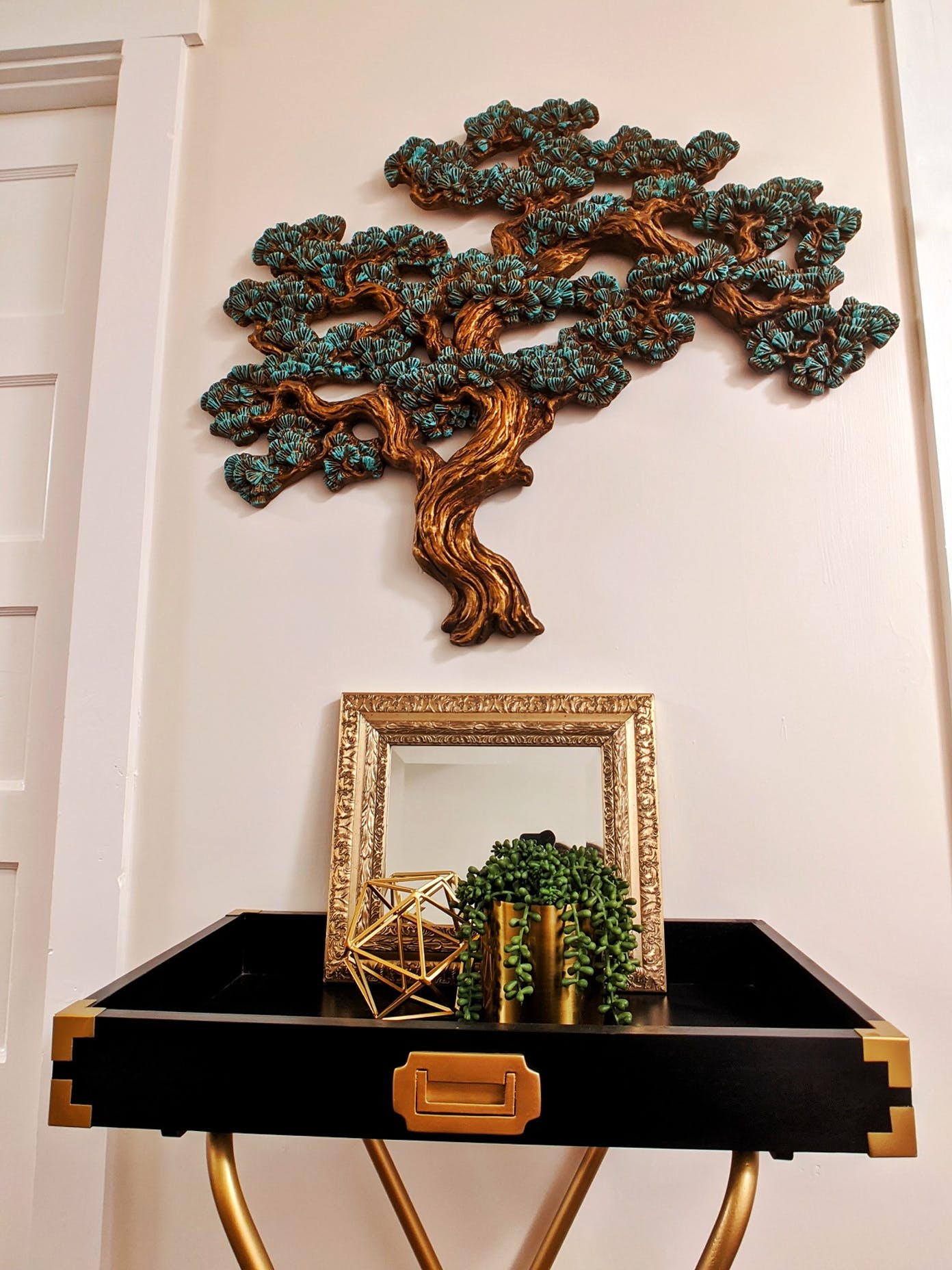 A table with a mirror and a tree on the wall above it