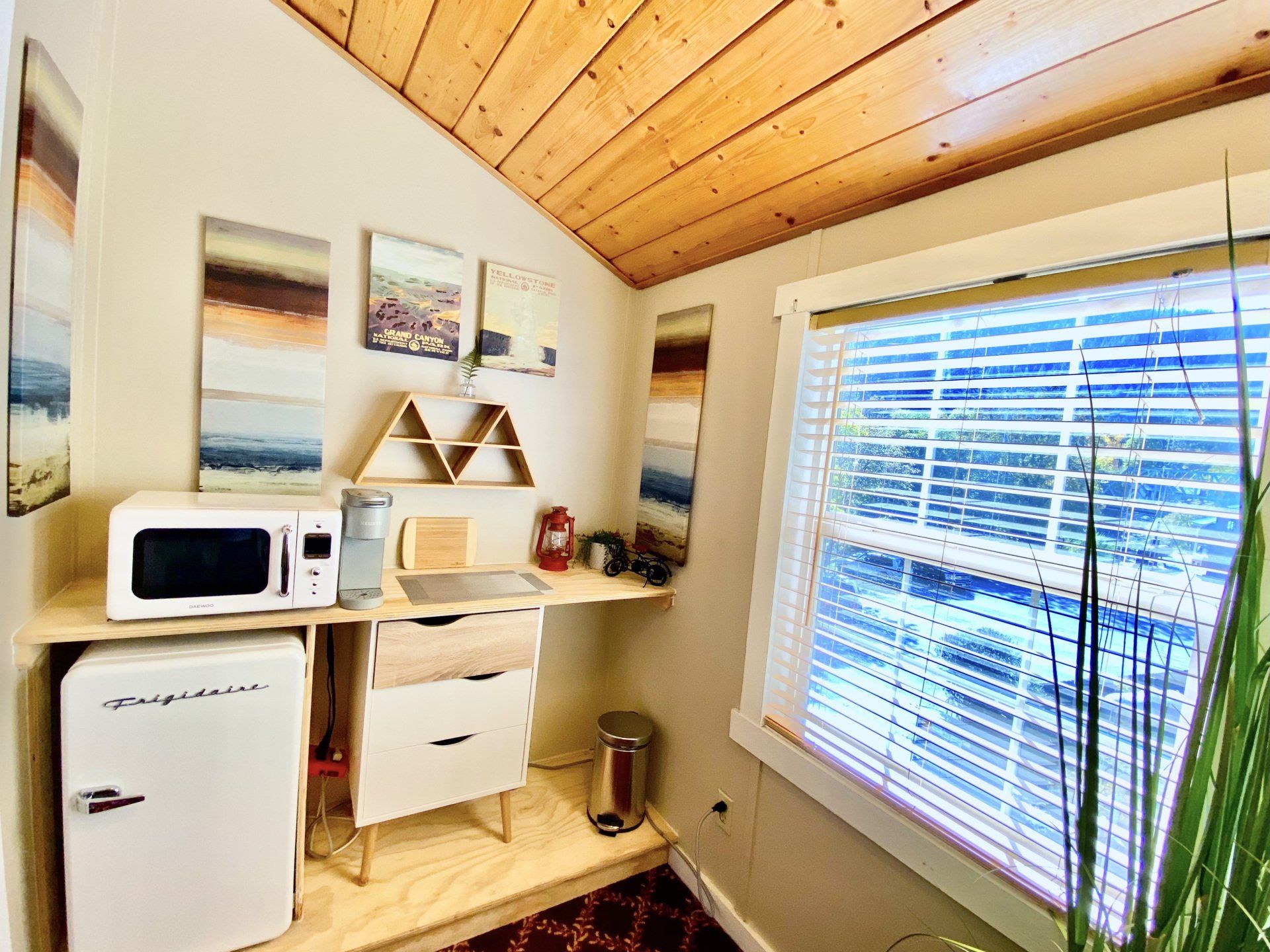 A small room with a microwave , refrigerator , desk and window.