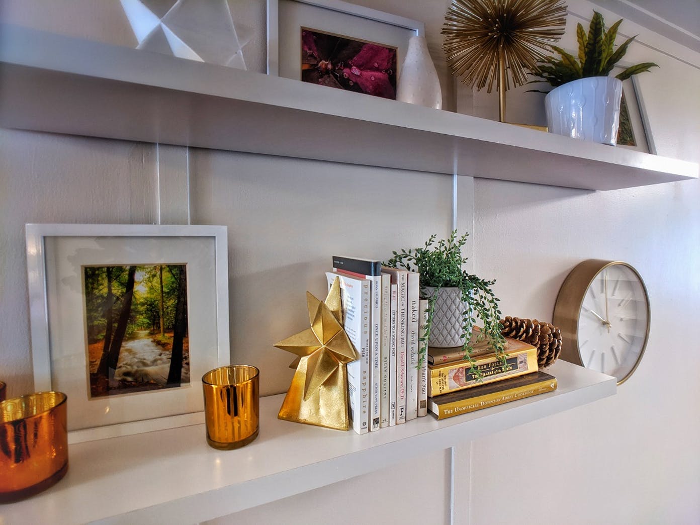 A shelf with books , pictures , candles and a clock on it
