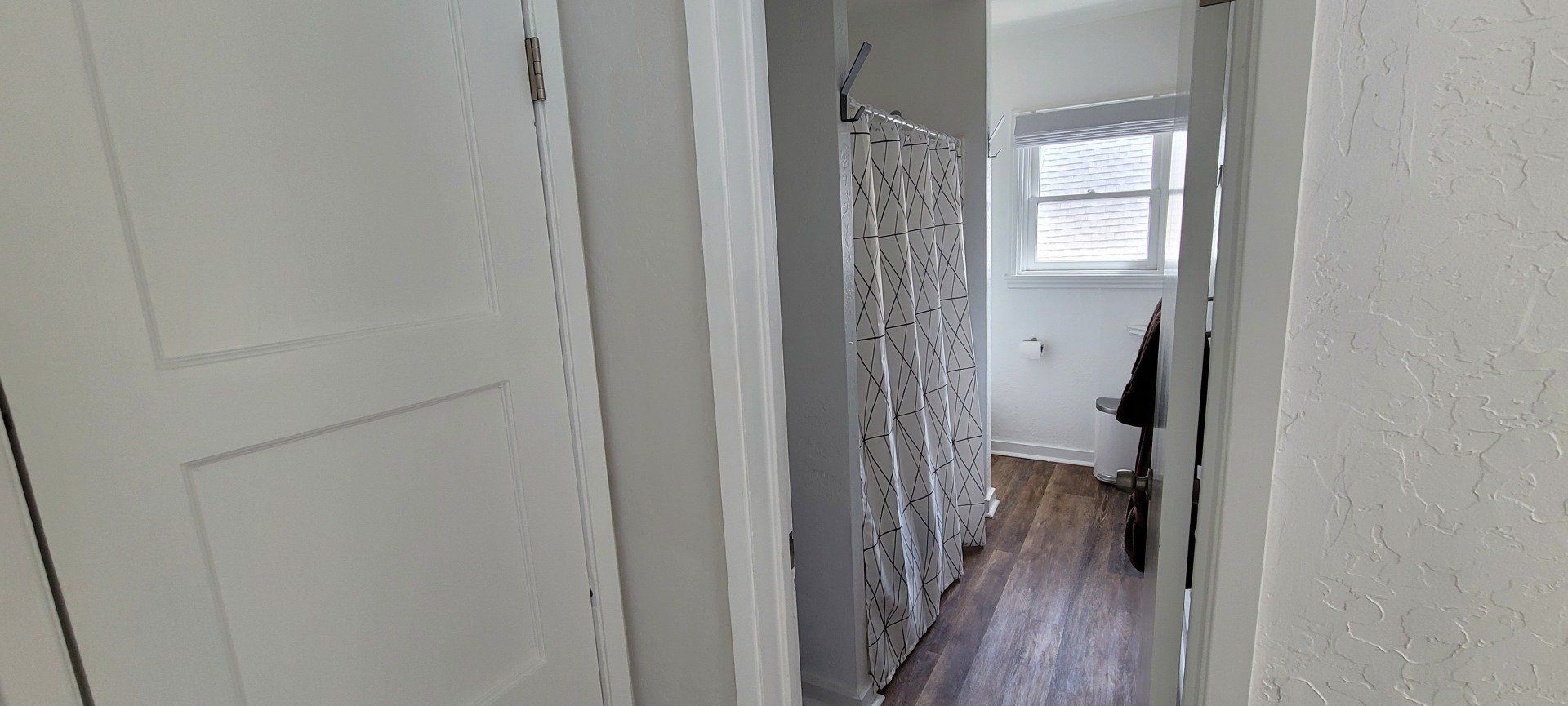 A hallway with white doors leading to a bathroom and a window.