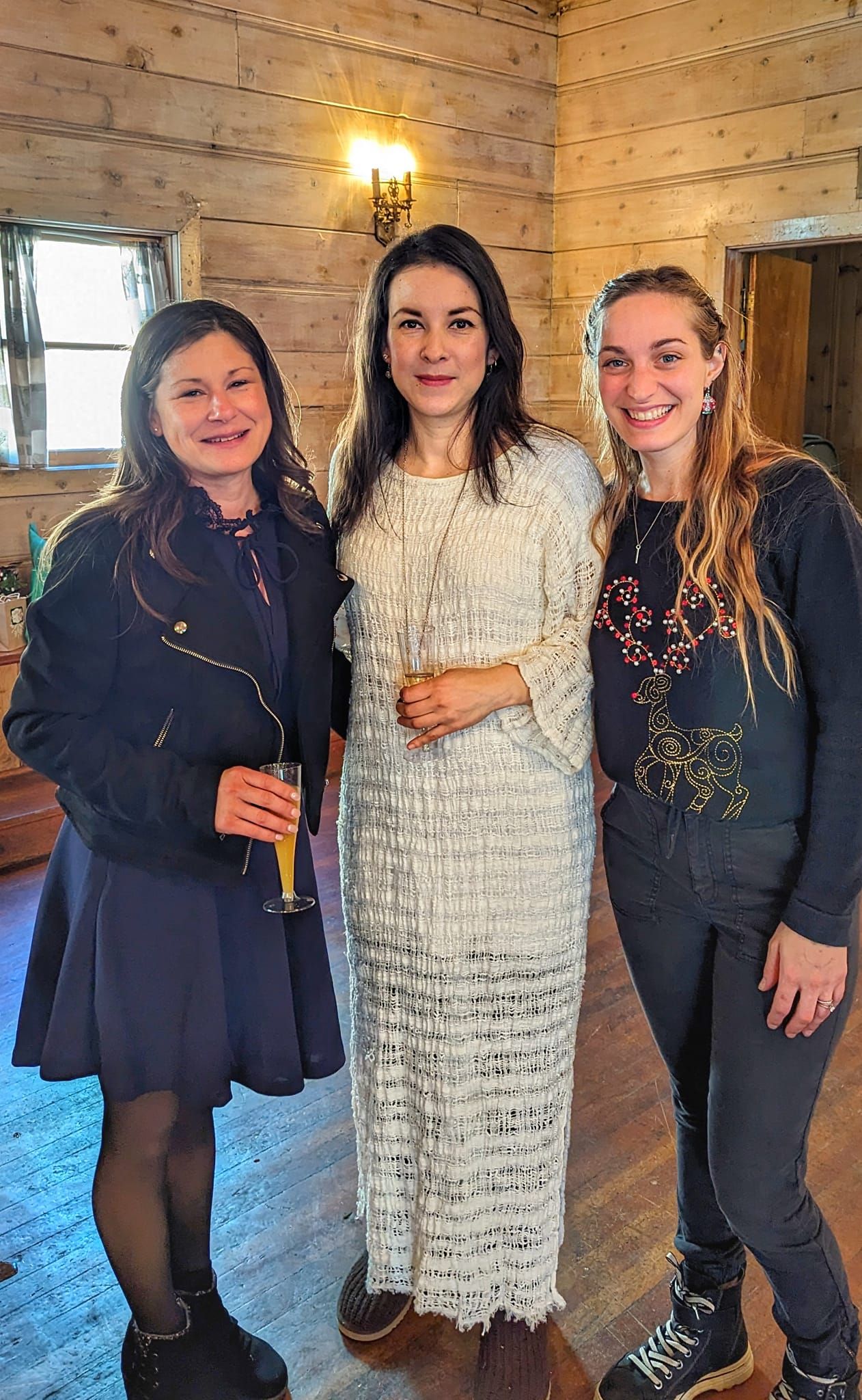 Three women are posing for a picture in a room . one of the women is wearing a white dress.