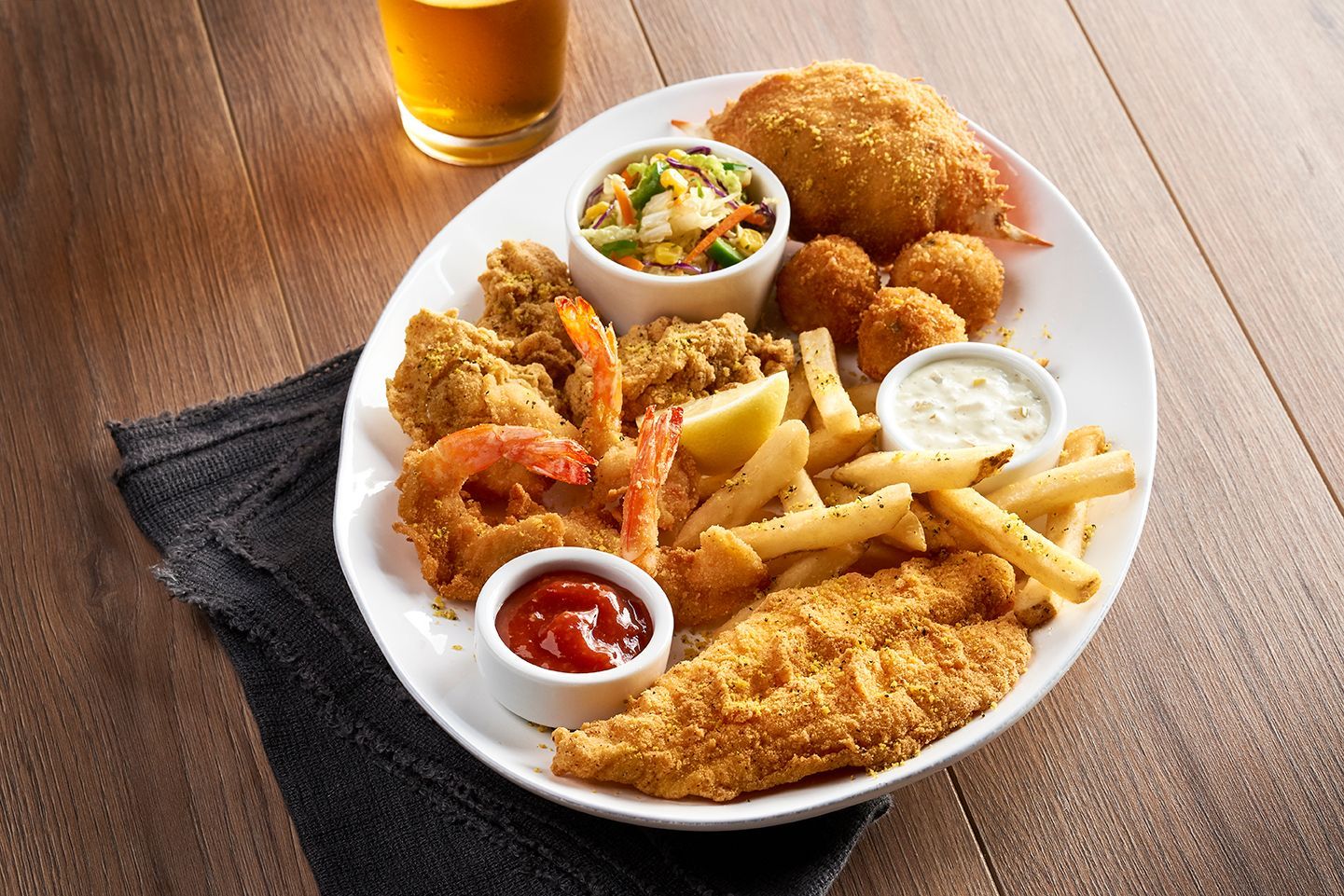 A plate of food with shrimp , french fries and coleslaw next to a glass of beer