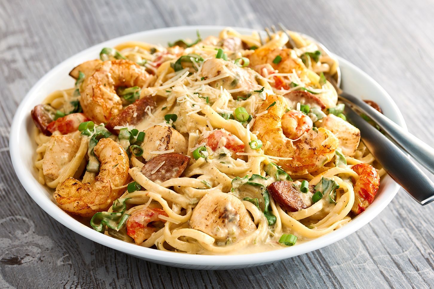 A bowl of pasta with shrimp and sausage with a fork in it