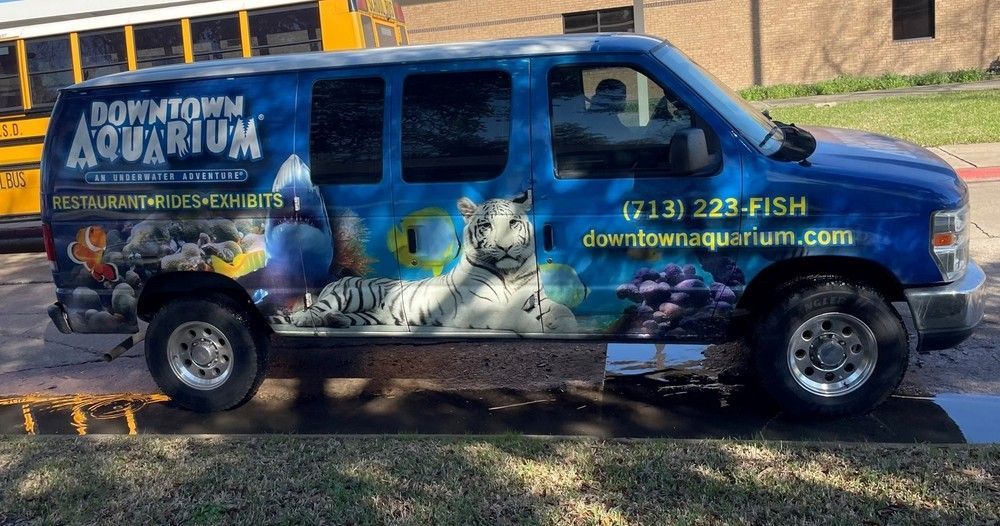 A downtown aquarium van is parked in front of a school bus