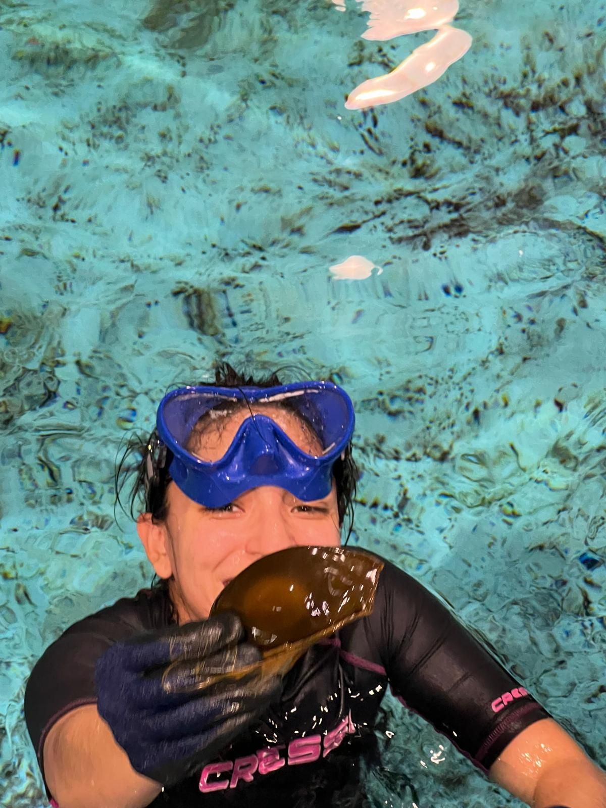 A woman wearing a cressi wetsuit is holding a shark egg called a mermaid purse