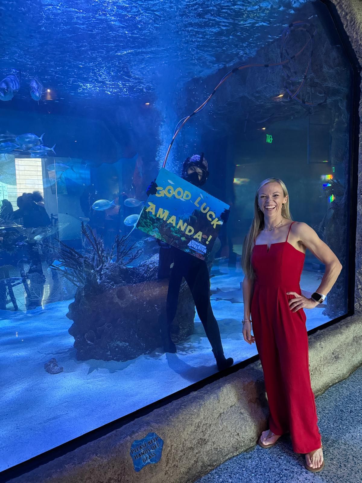 A woman in a red jumpsuit is standing in front of an aquarium