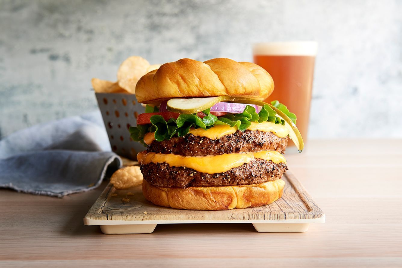 A hamburger is sitting on a wooden cutting board next to a glass of beer