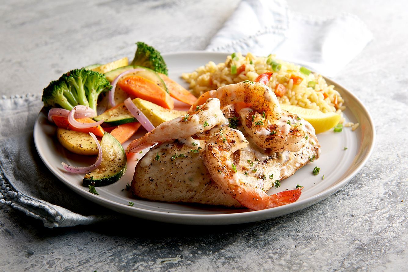A white plate topped with fish shrimp and rice and vegetables