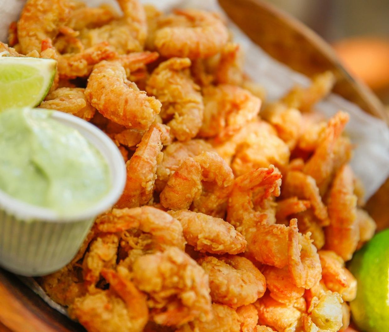 A bowl of fried shrimp next to a container of green sauce