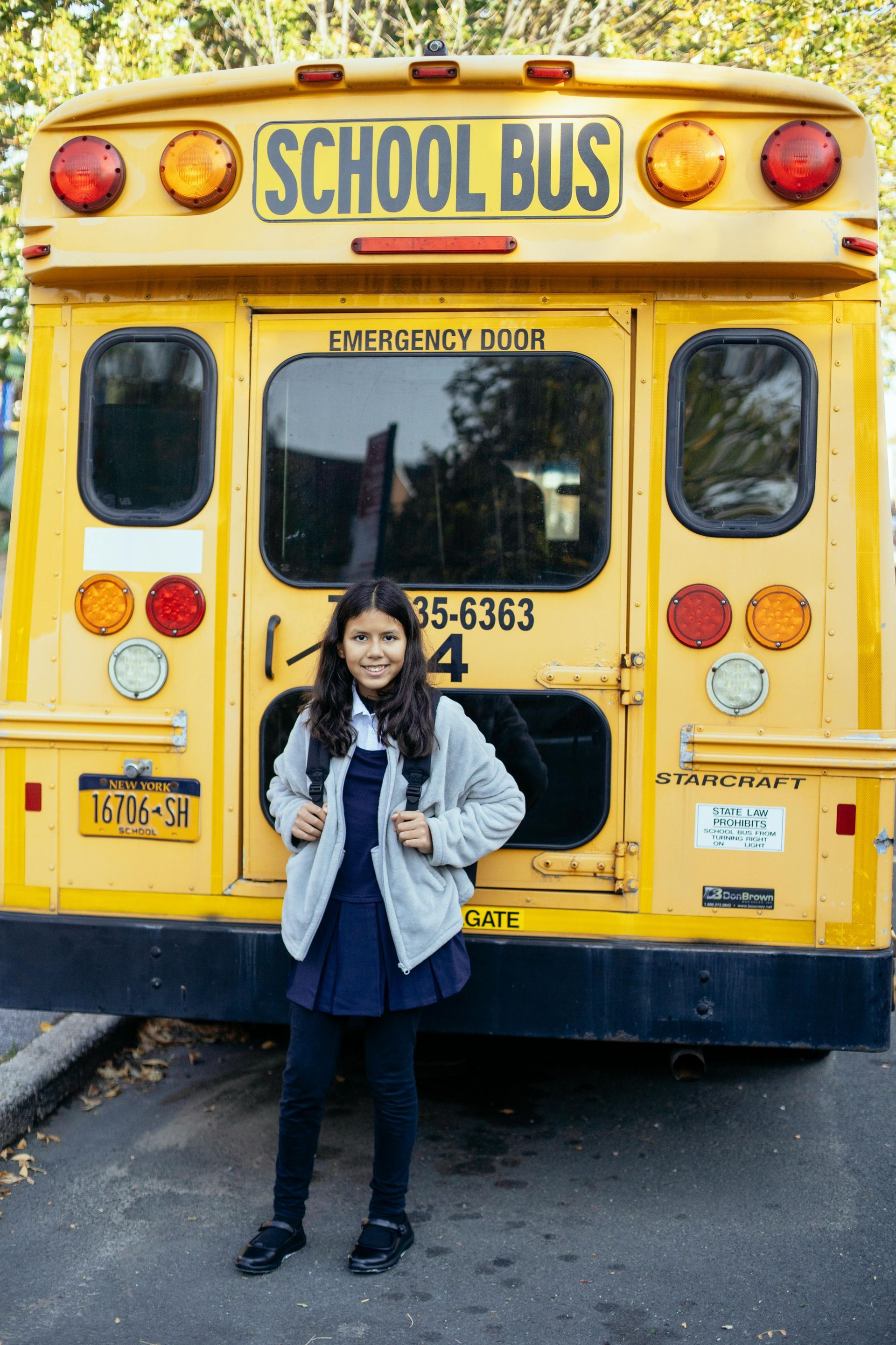 A girl stands in front of a yellow school bus