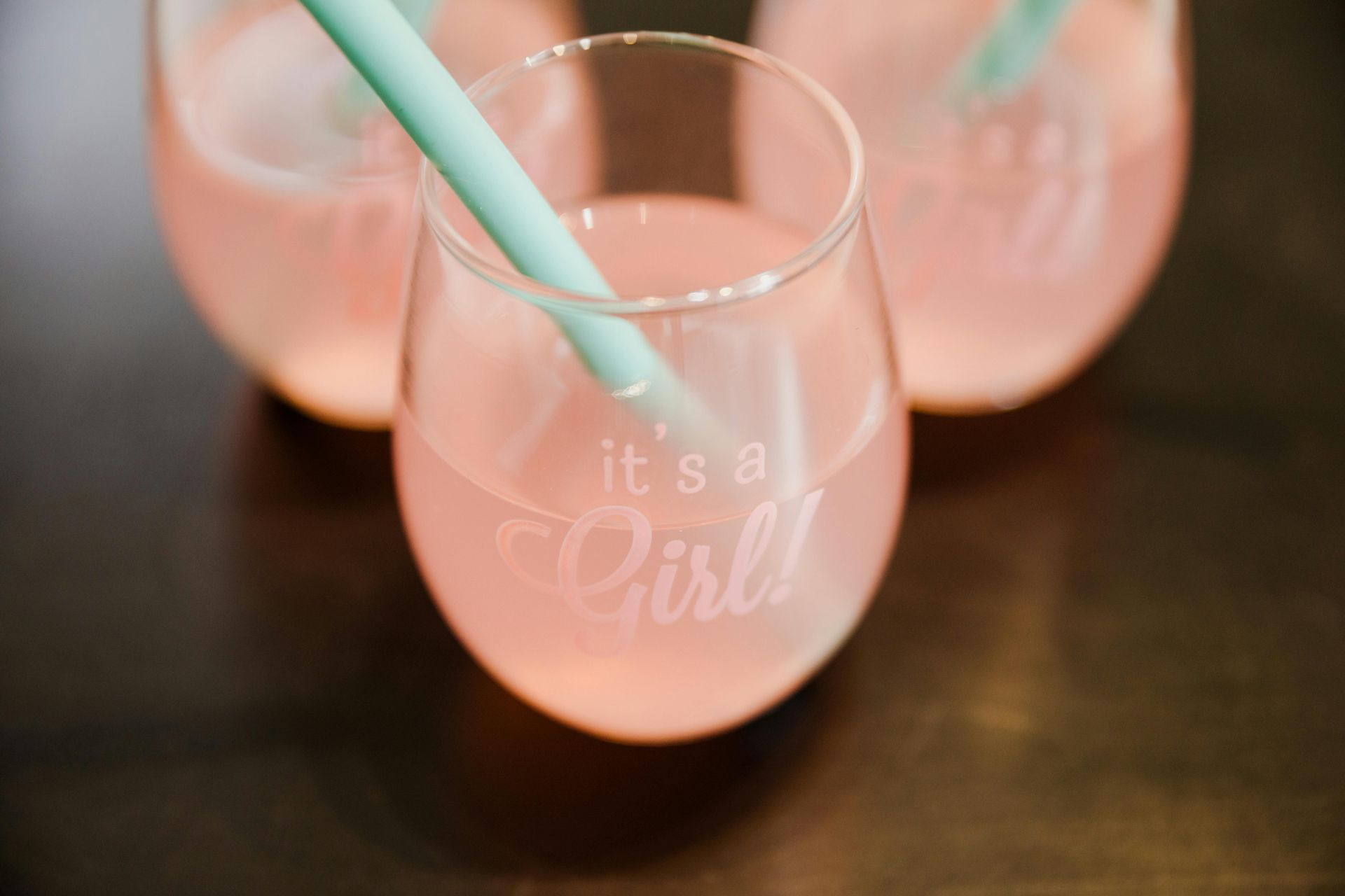 Three stemless glasses with pink liquid and straws, one saying