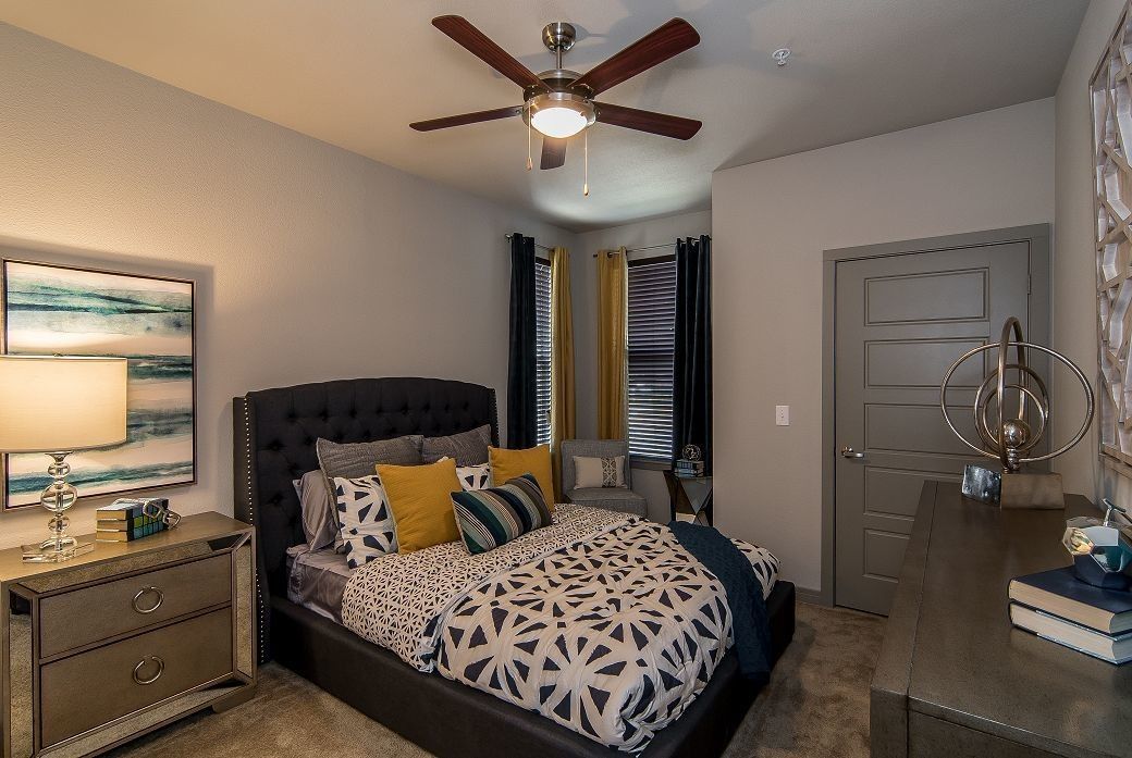 Bedroom with a dark tufted bed, two nightstands, dresser, and windows with navy and mustard curtains.