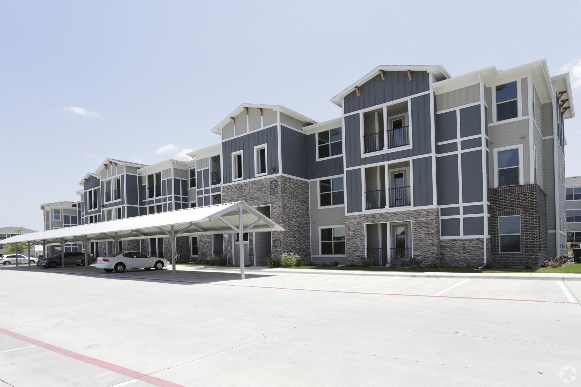 Exterior view of a modern apartment building with a long covered parking area.